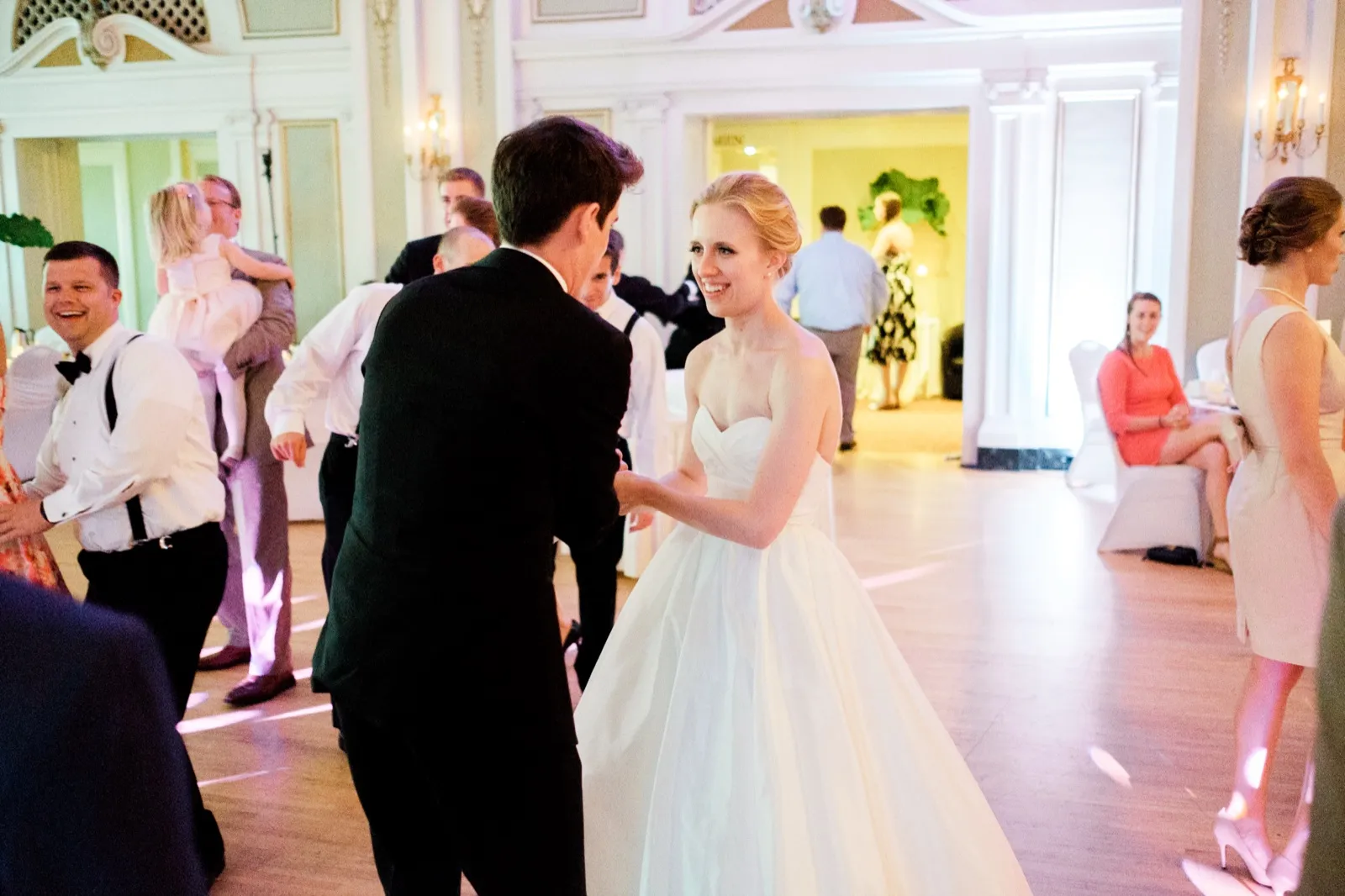 The bride smiles over her shoulder mid-spin on the open dance floor with the groom in the ornate Greysolon Ballroom while guests laugh and watch from the edges — Tim Larsen Photography, Duluth MN