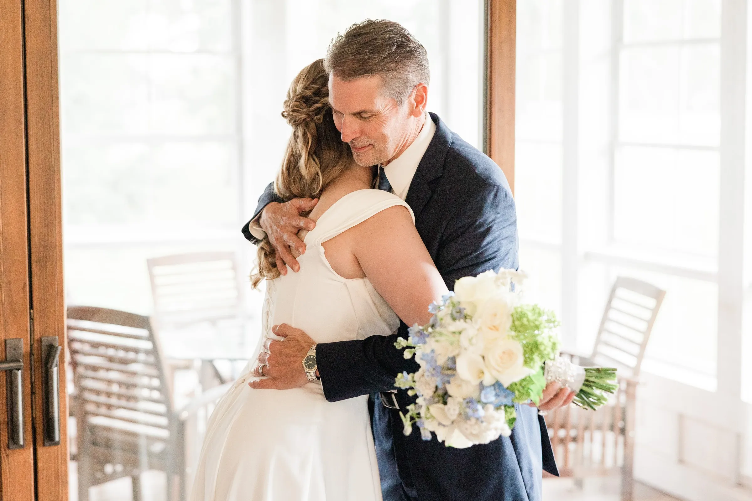 Lauren embraces a man in a blue suit beside a bright window — Tim Larsen Photography, Brainerd Lakes MN
