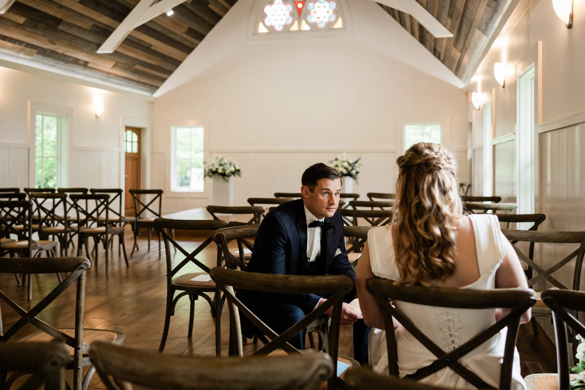 Lauren and Noah sit among the empty chairs beneath the Chapel’s timber ceiling and stained glass — Tim Larsen Photography, Brainerd Lakes MN