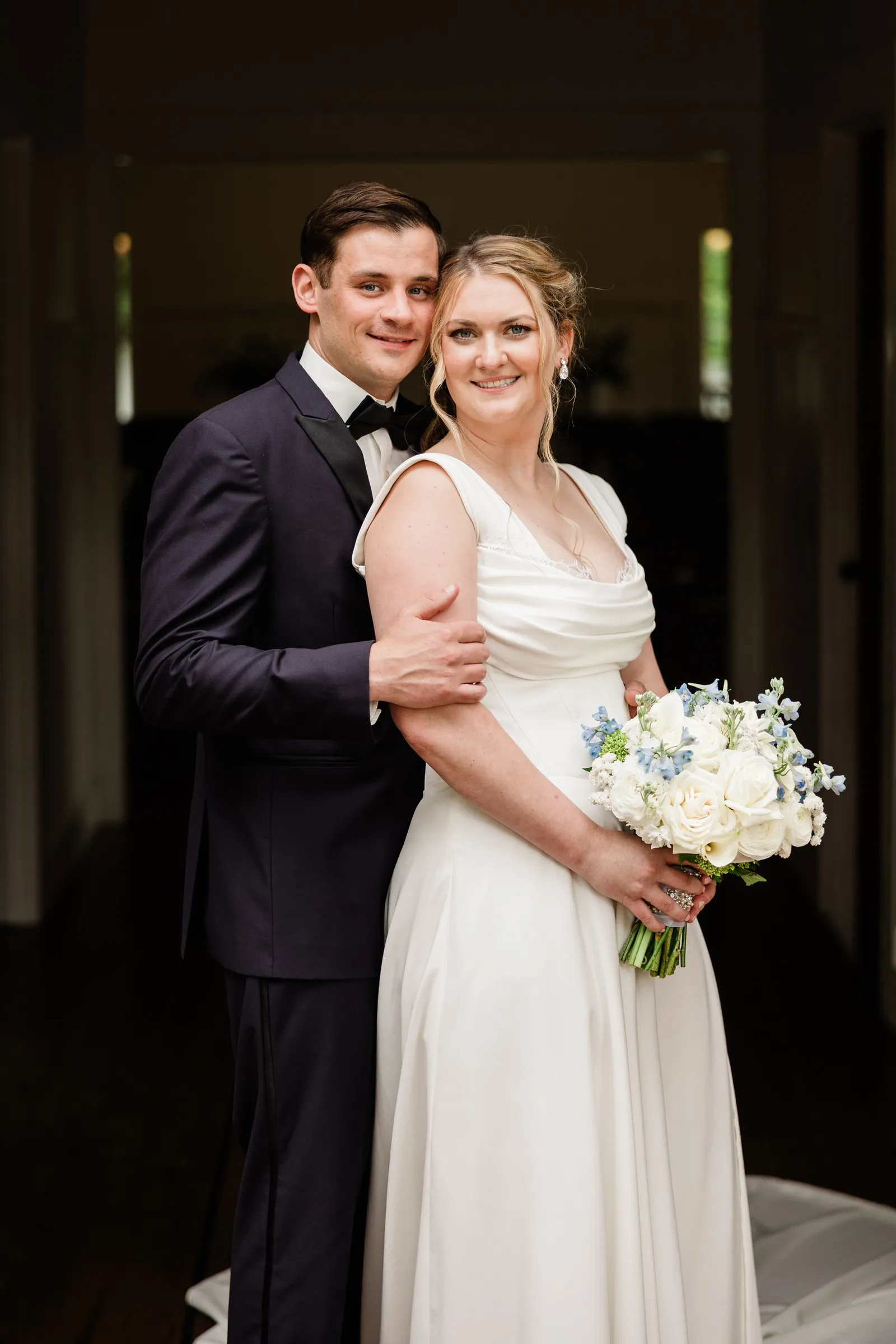 Lauren and Noah hold each other in the Chapel doorway with her blue and white bouquet — Tim Larsen Photography, Brainerd Lakes MN