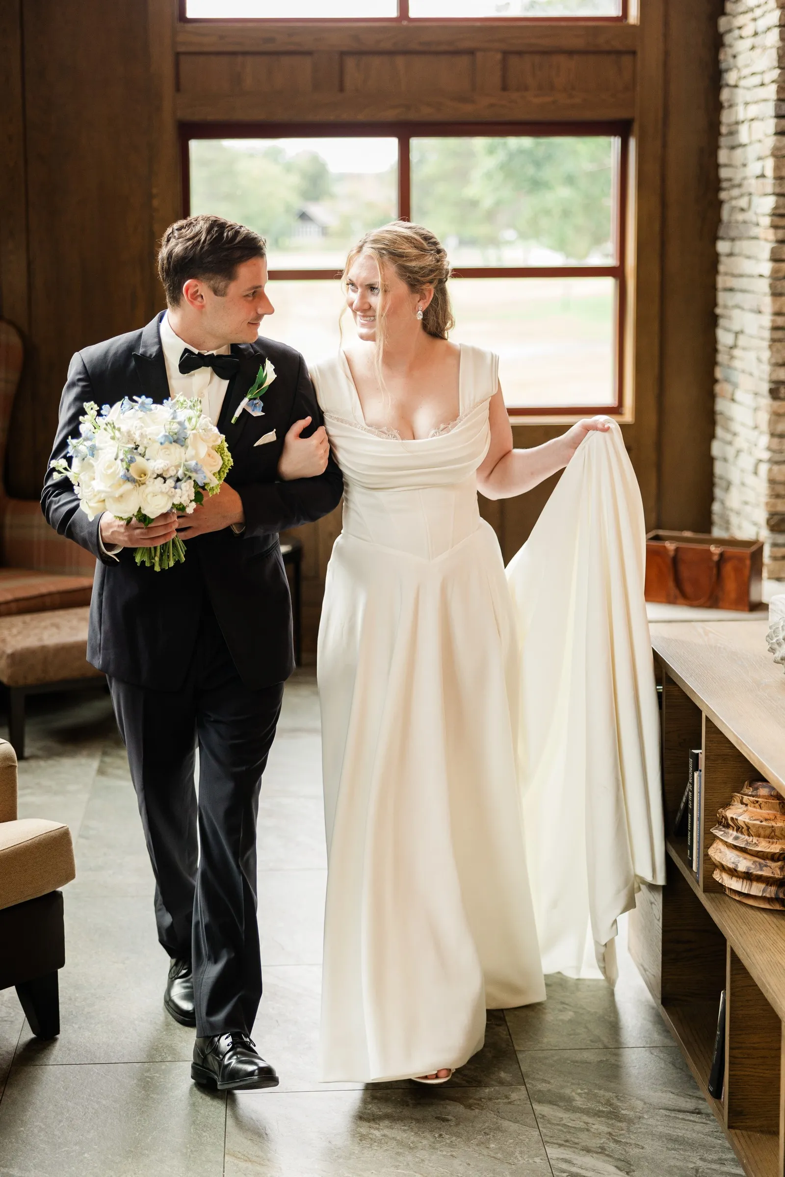 Lauren and Noah walk arm in arm through a window-lit lodge room — Tim Larsen Photography, Brainerd Lakes MN
