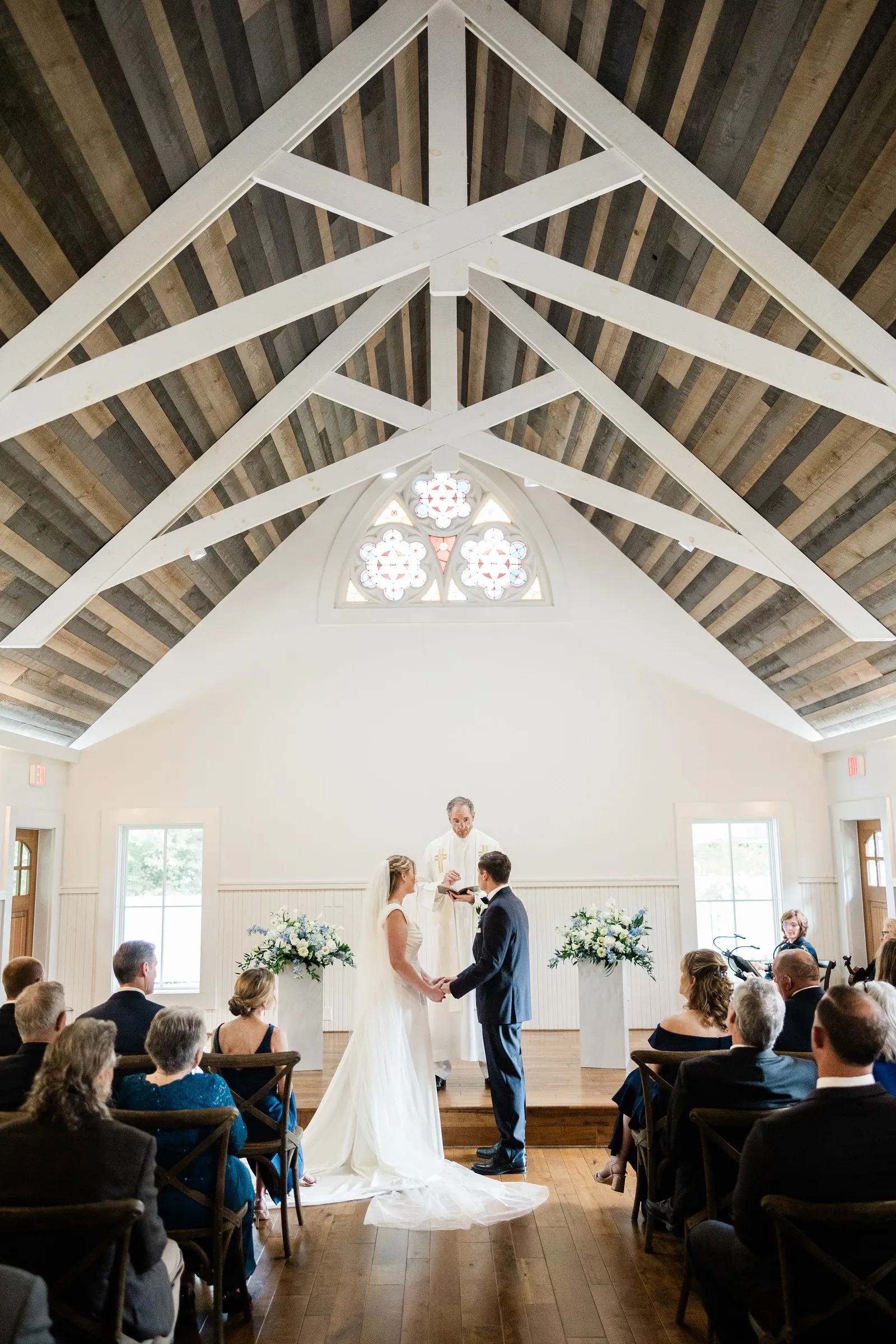 Lauren and Noah’s ceremony beneath the white timber trusses and stained glass of the Chapel — Tim Larsen Photography, Brainerd Lakes MN