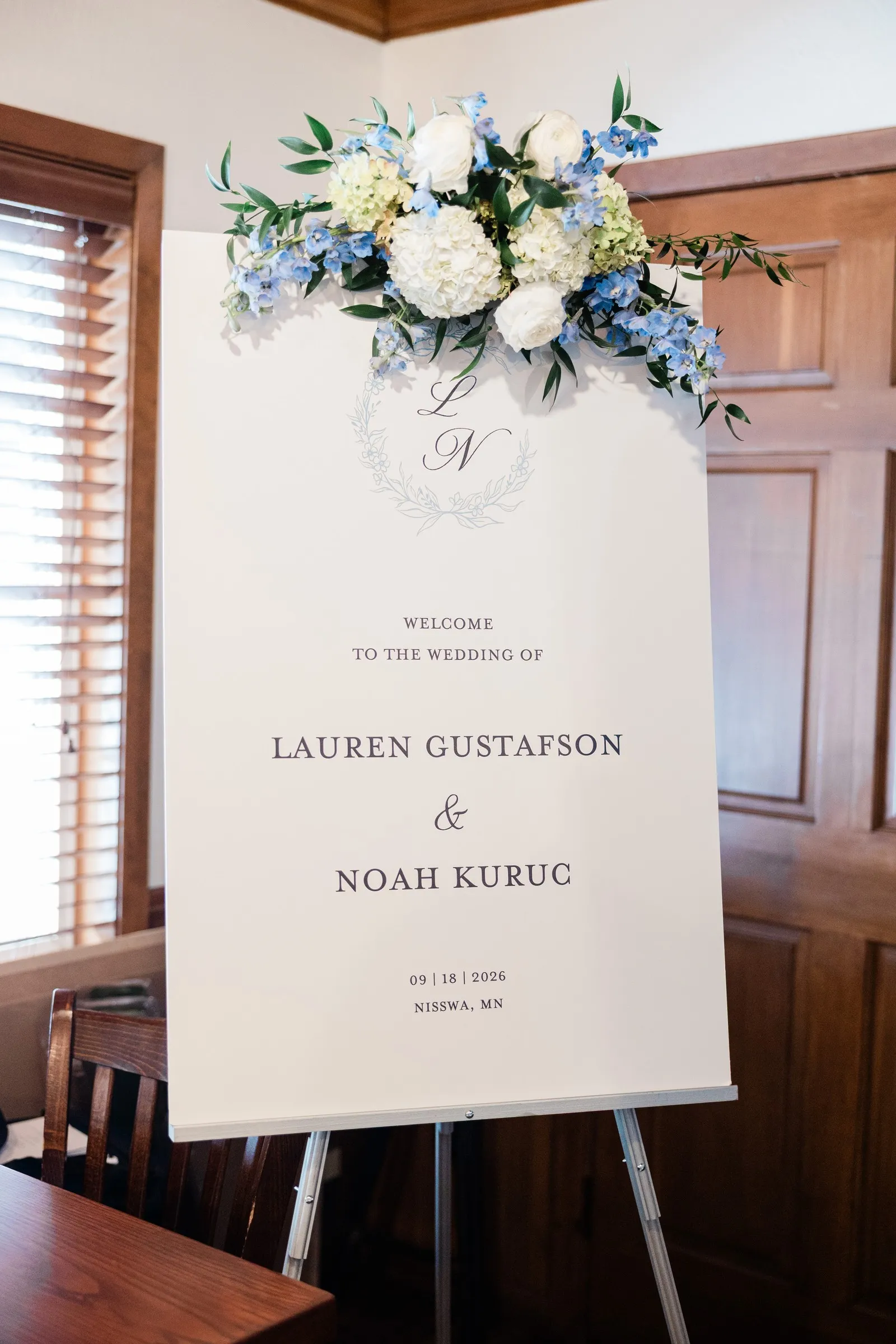 A welcome sign for Lauren and Noah’s September 18 wedding topped with white and blue flowers — Tim Larsen Photography, Brainerd Lakes MN