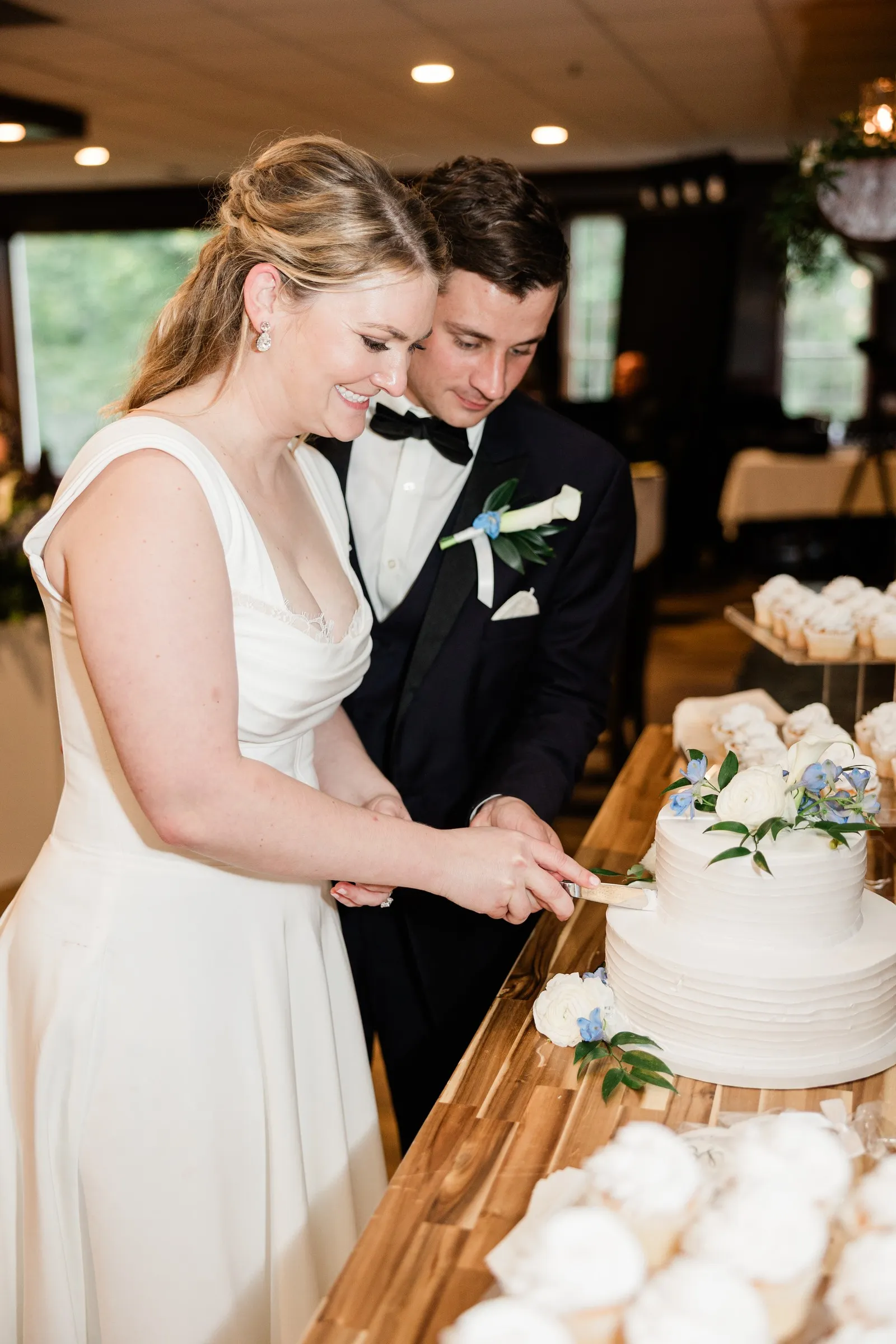 Lauren and Noah cut their white wedding cake decorated with blue and white flowers — Tim Larsen Photography, Brainerd Lakes MN