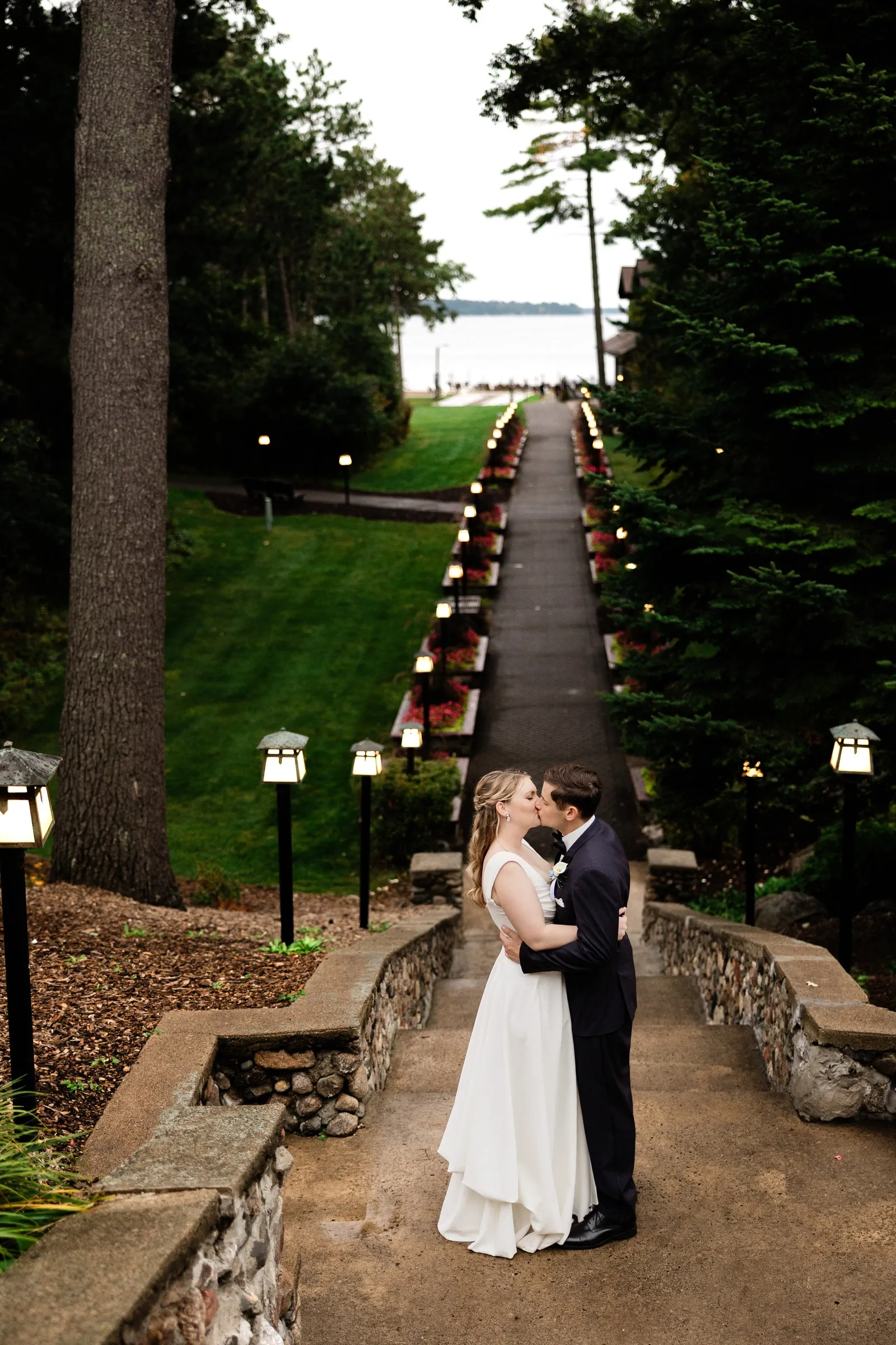 Lauren and Noah kiss on the Grand View Lodge stone staircase with the garden path and Gull Lake beyond — Tim Larsen Photography, Brainerd Lakes MN