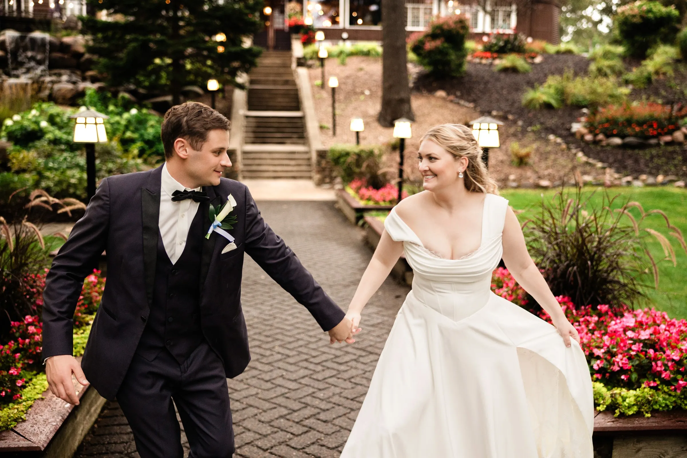 Lauren and Noah smile at each other while walking hand in hand along the lodge garden path — Tim Larsen Photography, Brainerd Lakes MN