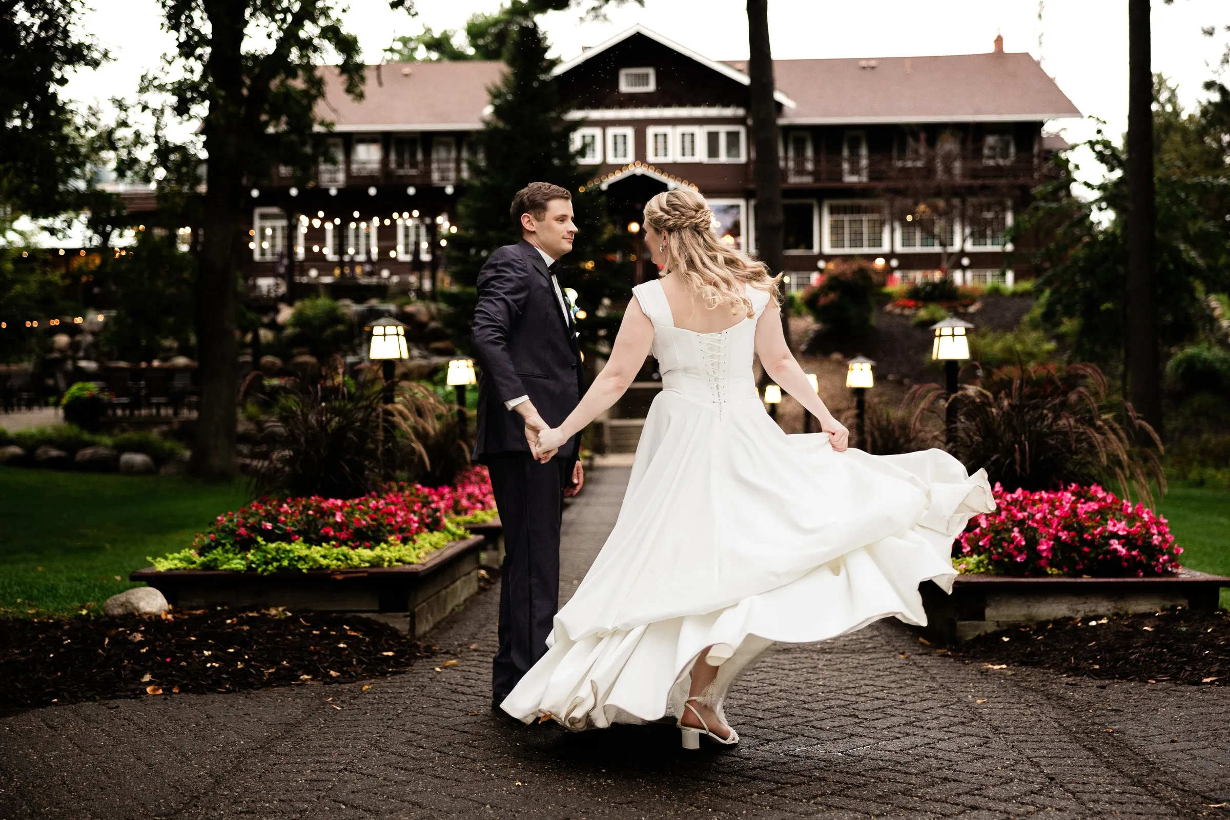 Lauren twirls while holding Noah’s hand on the flower-lined path in front of Grand View Lodge — Tim Larsen Photography, Brainerd Lakes MN