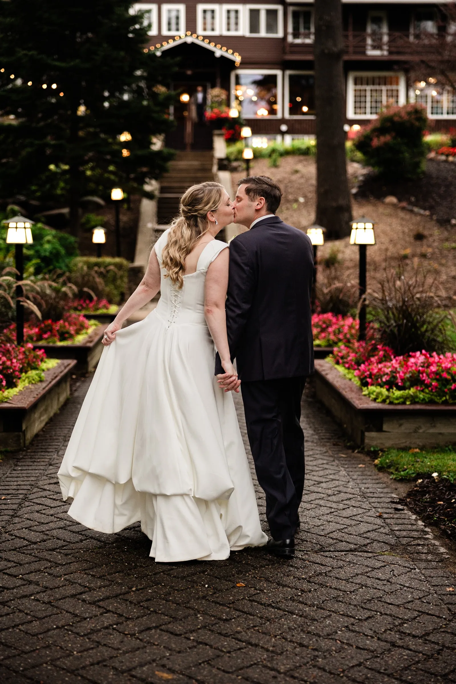 Lauren and Noah hold hands and turn toward each other for a kiss on the garden path — Tim Larsen Photography, Brainerd Lakes MN