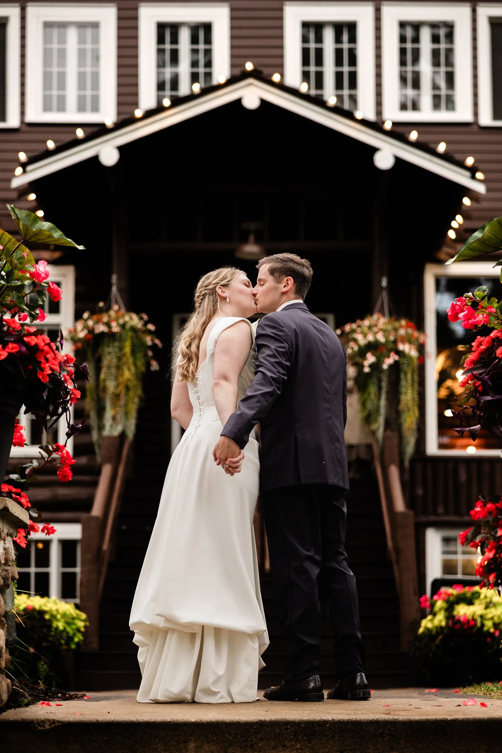 Lauren and Noah kiss beneath the lights of Grand View Lodge, framed by flowers — Tim Larsen Photography, Brainerd Lakes MN