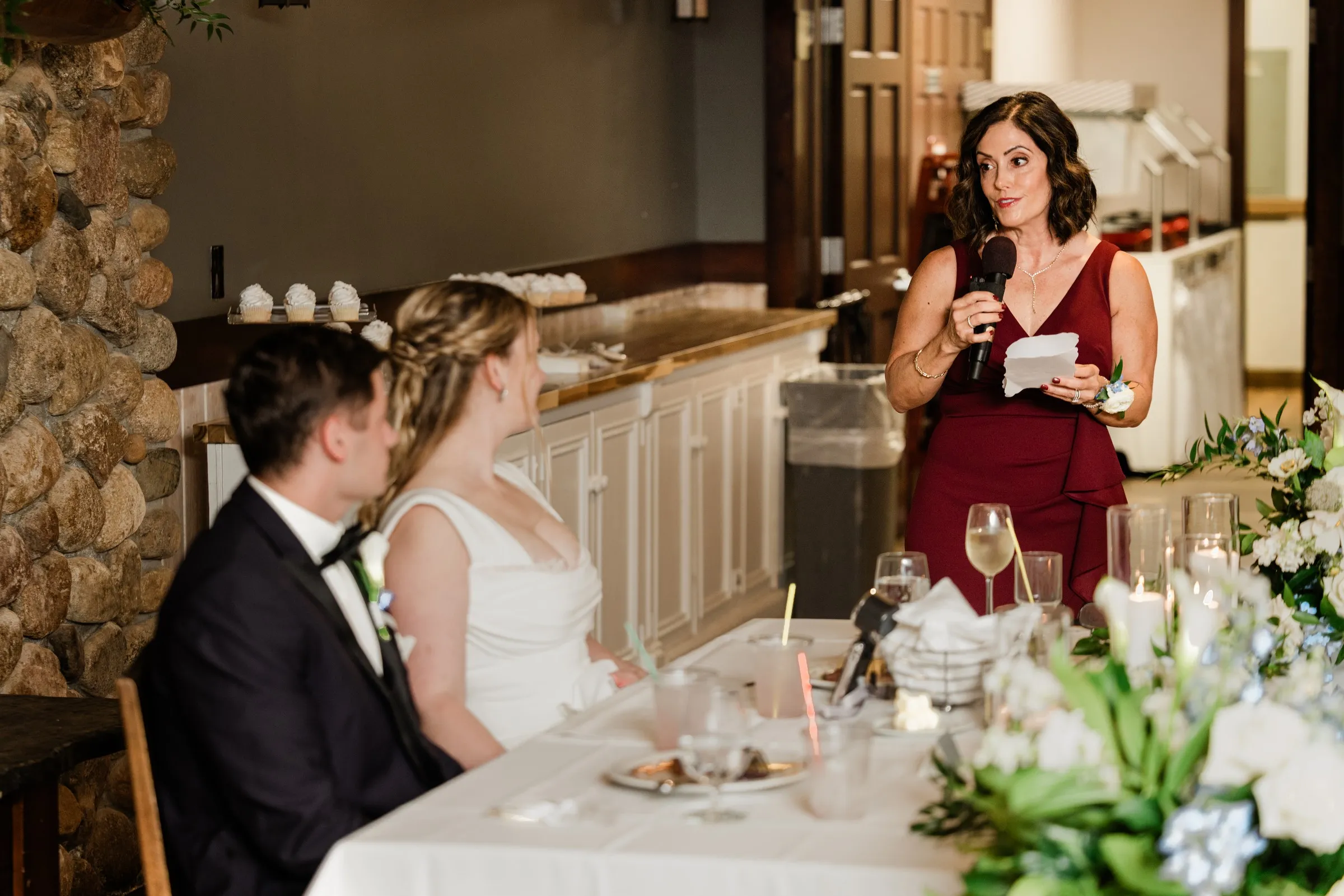 A guest in a burgundy dress gives a toast as Lauren and Noah watch from the head table — Tim Larsen Photography, Brainerd Lakes MN