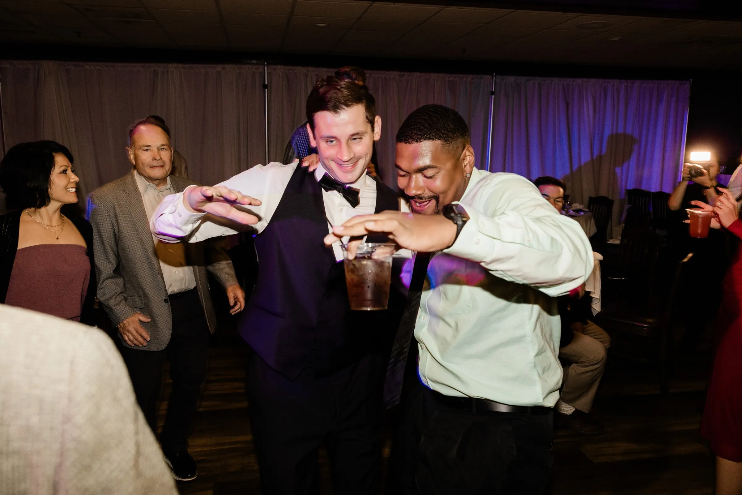 Noah and a friend laugh together on the dance floor with drinks in hand — Tim Larsen Photography, Brainerd Lakes MN