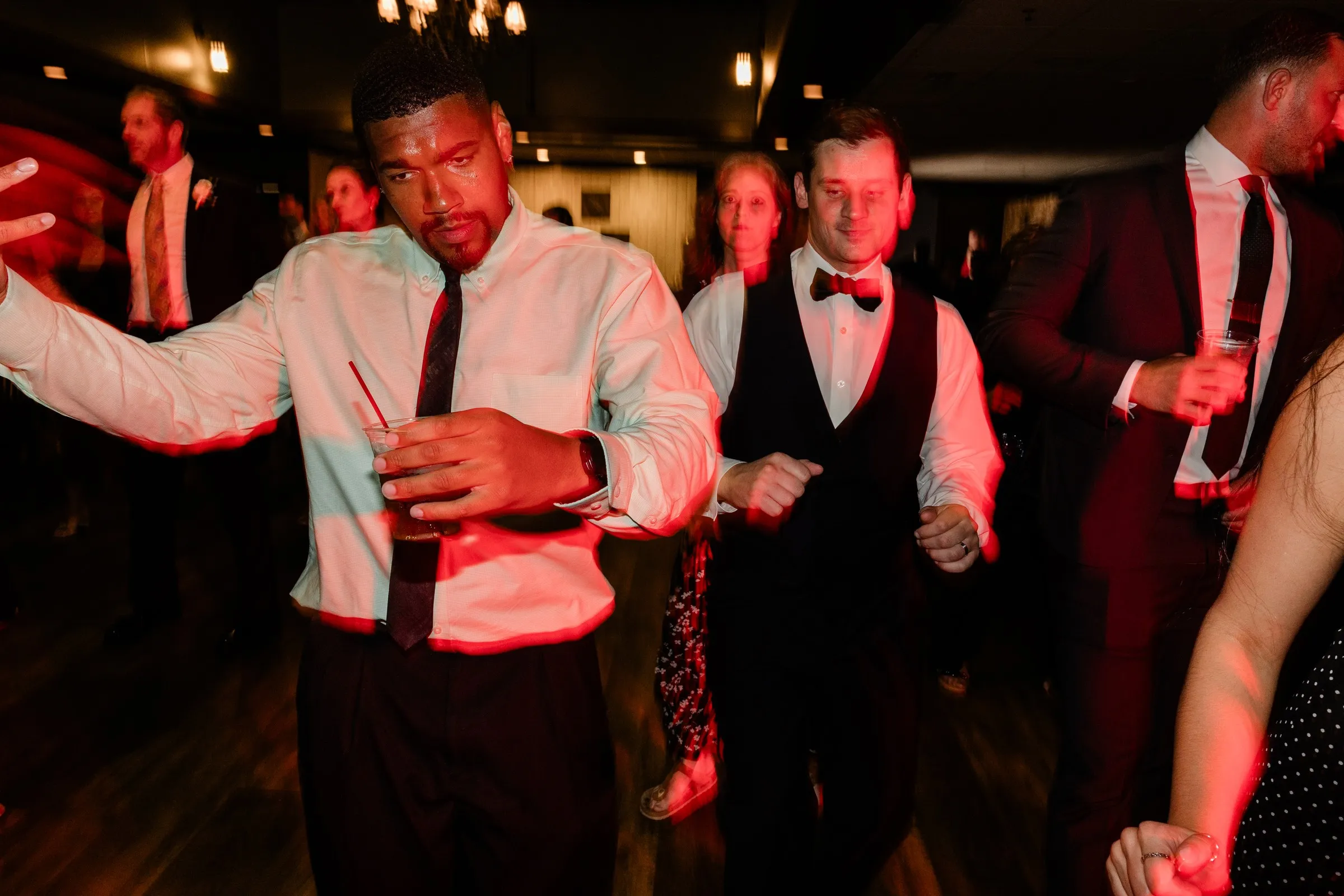 Guests dance with drinks in hand under red reception lighting — Tim Larsen Photography, Brainerd Lakes MN