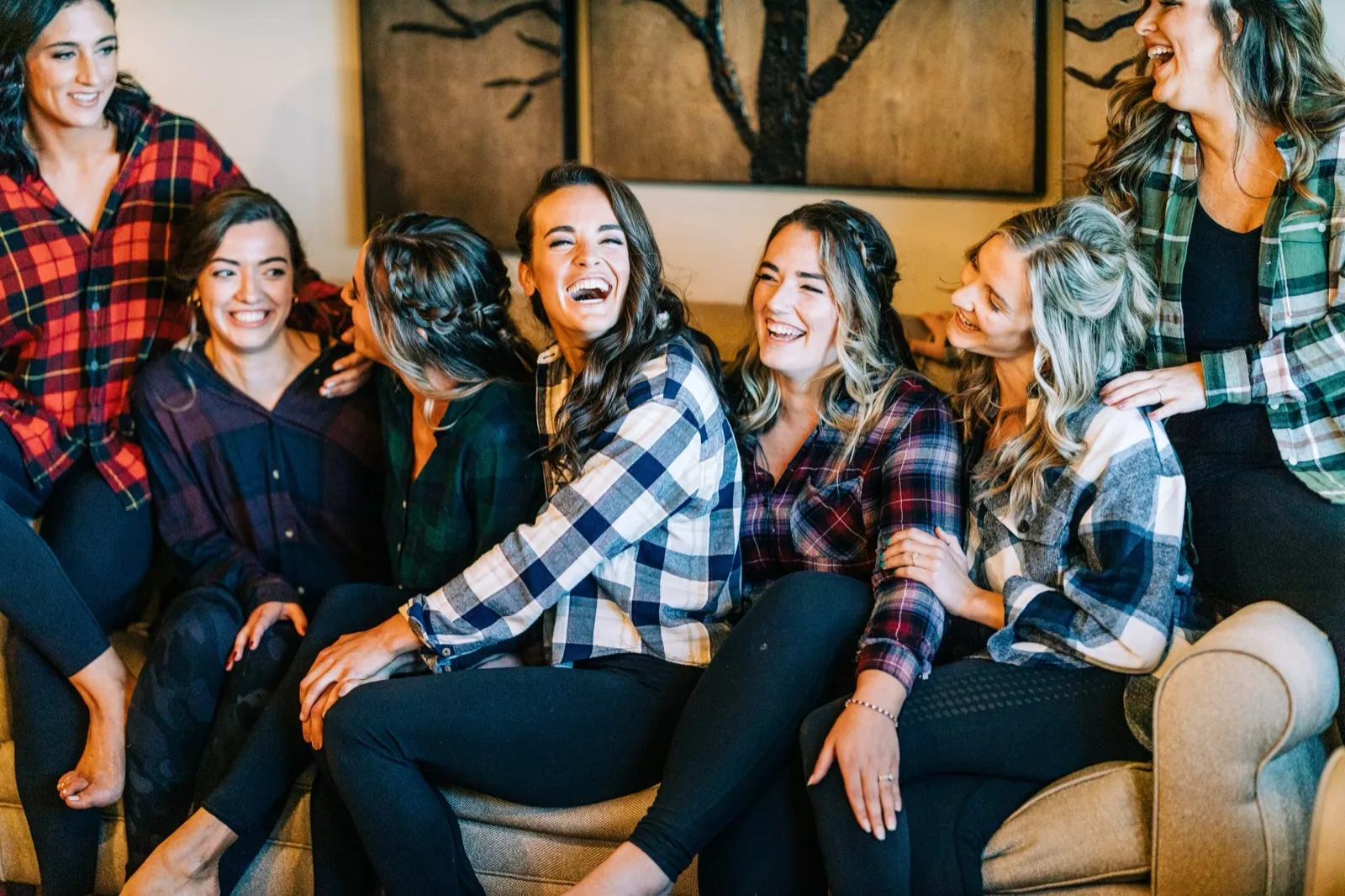 Madison laughs in the center of a couch surrounded by six bridesmaids in matching plaid flannel shirts at Madden's — Tim Larsen Photography, Brainerd Lakes MN