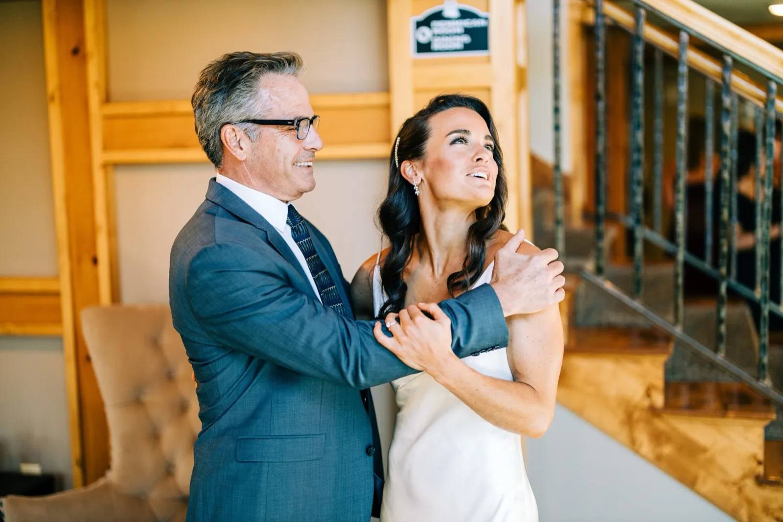 Madison laughs while embracing her father, both looking upward, near the lodge staircase — Tim Larsen Photography, Brainerd Lakes MN