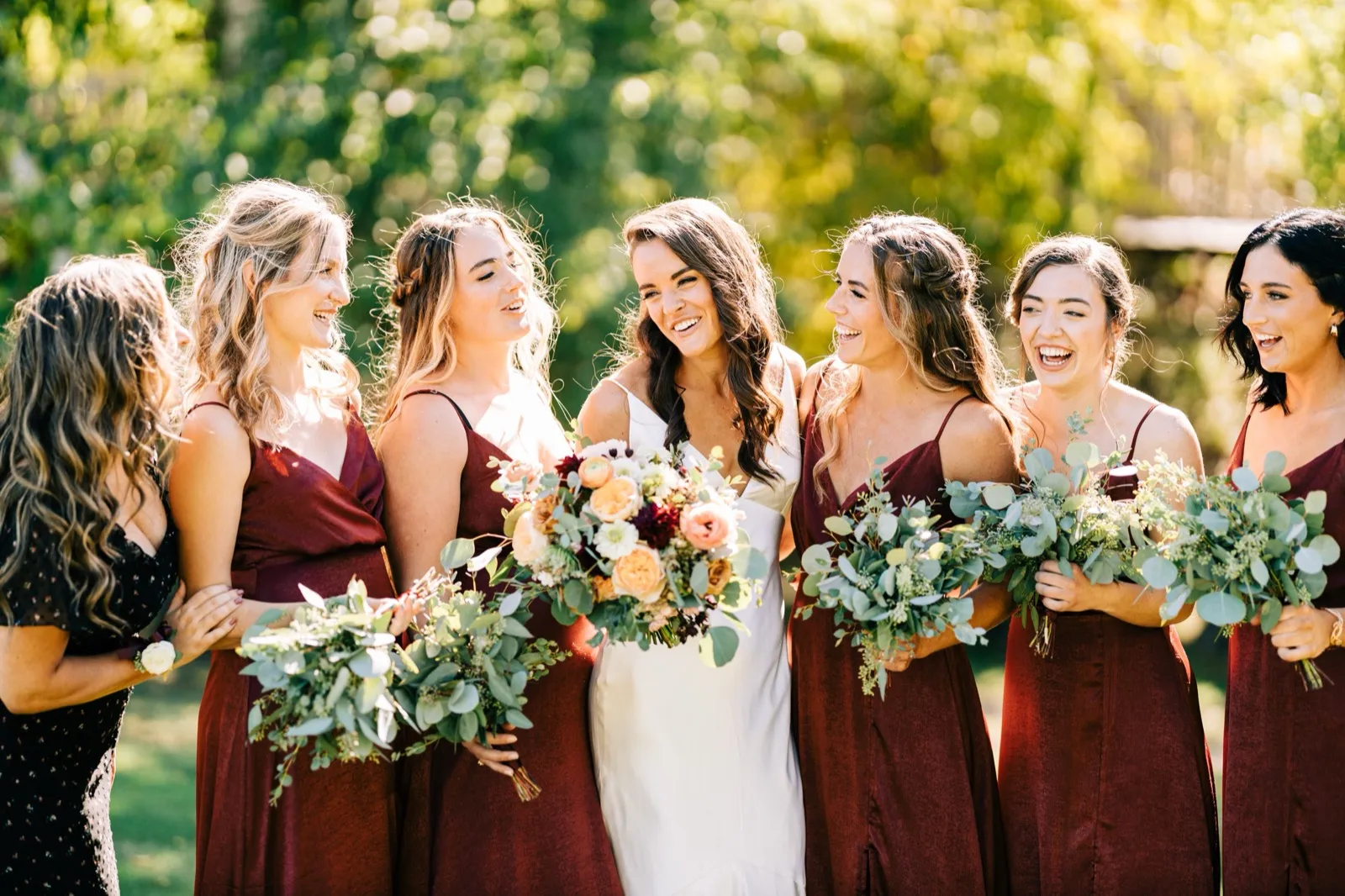 Madison at the center of her bridesmaids in burgundy, all laughing with autumnal bouquets in afternoon backlight — Tim Larsen Photography, Brainerd Lakes MN