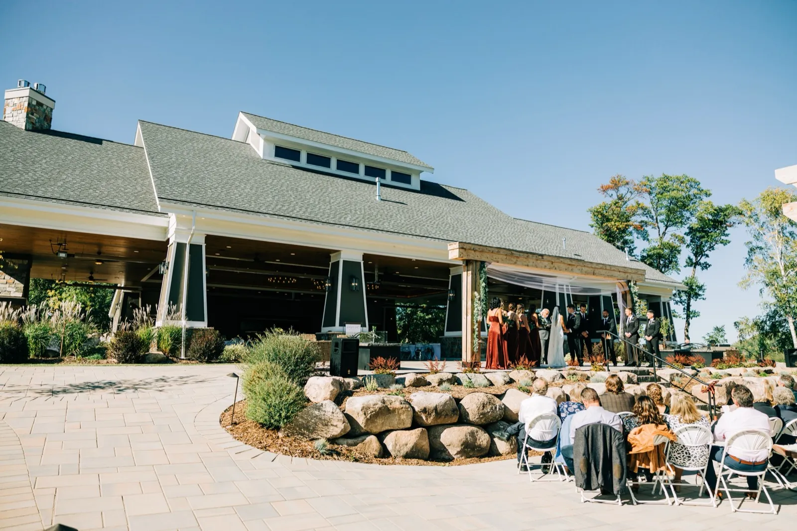 A wide view of the open-air Pavilion ceremony at Madden's on Gull Lake, the bridal party in burgundy under the draped timber pavilion — Tim Larsen Photography, Brainerd Lakes MN