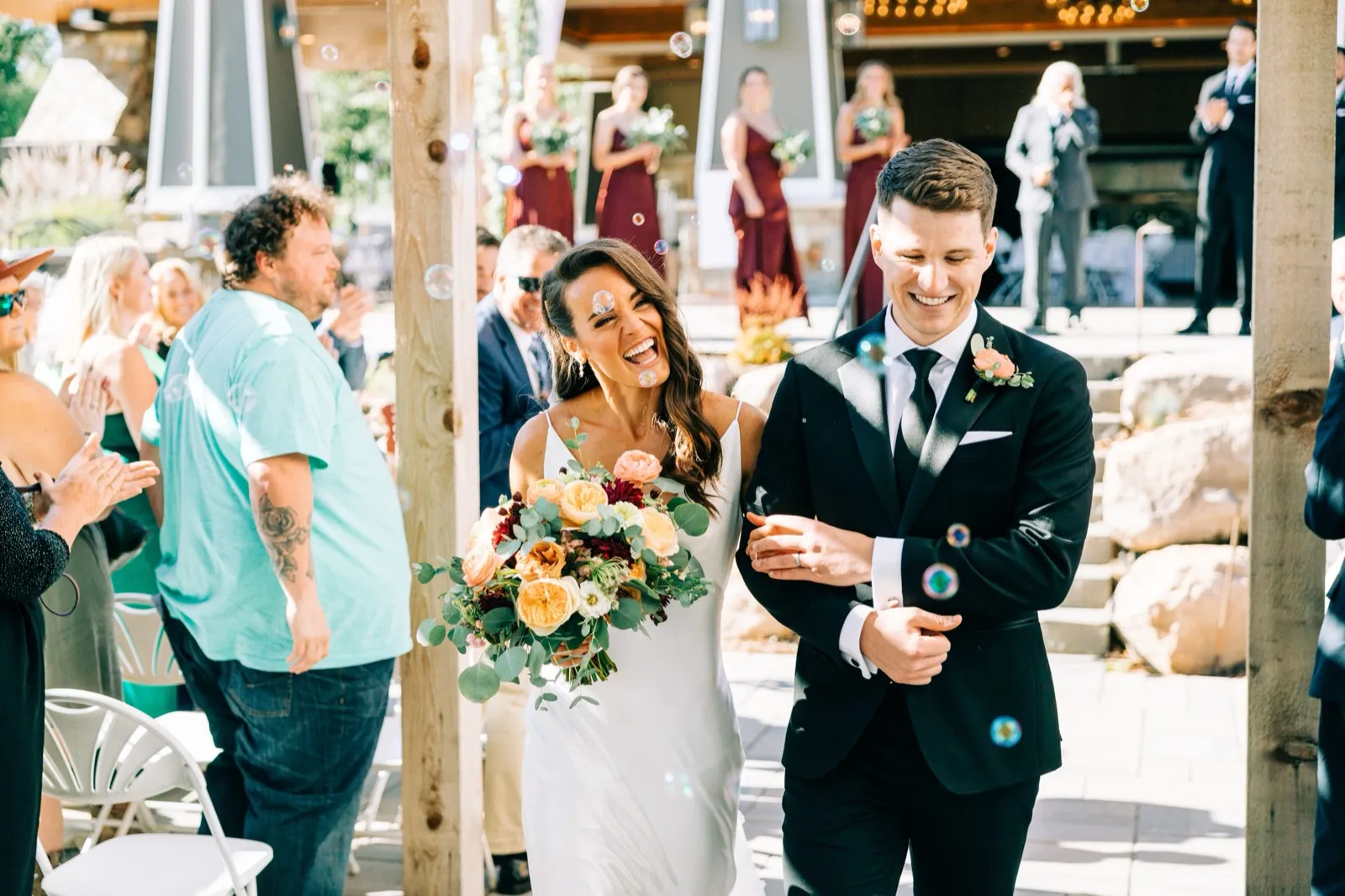 Madison laughs openly as she and Josh walk down the aisle through floating bubbles, the bridal party applauding behind them — Tim Larsen Photography, Brainerd Lakes MN