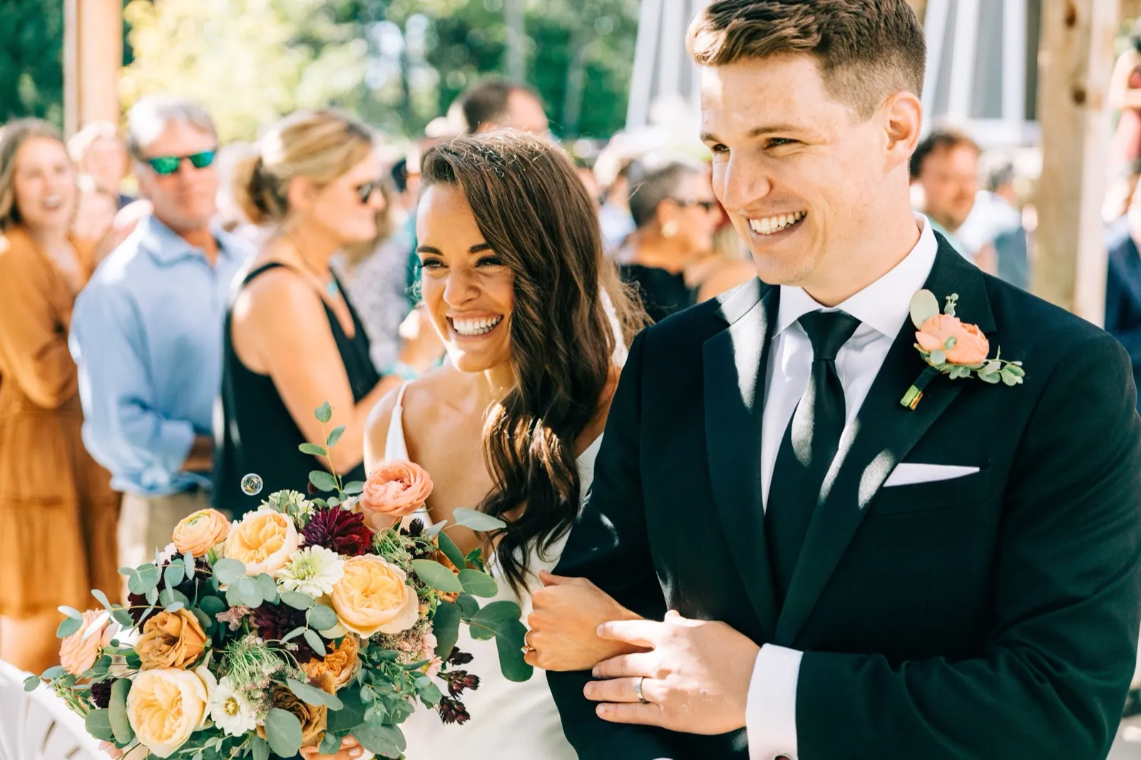 Madison and Josh laugh walking down the aisle just after the ceremony, her peach-and-burgundy bouquet at her side — Tim Larsen Photography, Brainerd Lakes MN