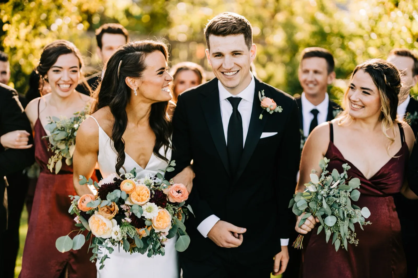 Madison laughs at Josh as their bridal party walks alongside them in warm afternoon light on a garden lawn at Madden's — Tim Larsen Photography, Brainerd Lakes MN