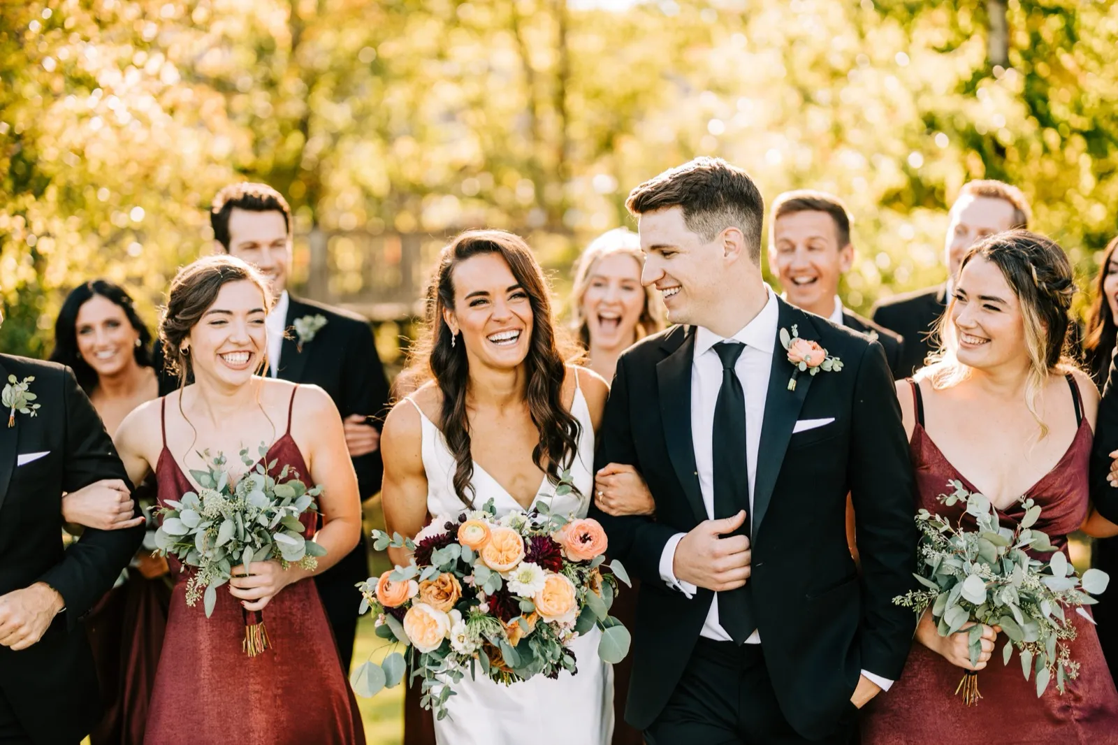 Madison and Josh walk arm-in-arm at the center of their bridal party, backlit autumn foliage glowing behind them — Tim Larsen Photography, Brainerd Lakes MN