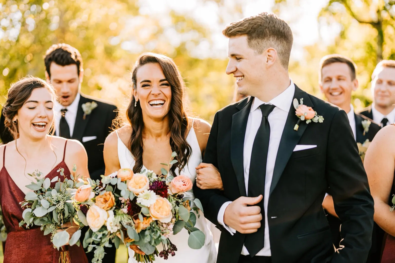 Madison laughs walking arm-in-arm with Josh, surrounded by their bridal party in warm afternoon backlight — Tim Larsen Photography, Brainerd Lakes MN