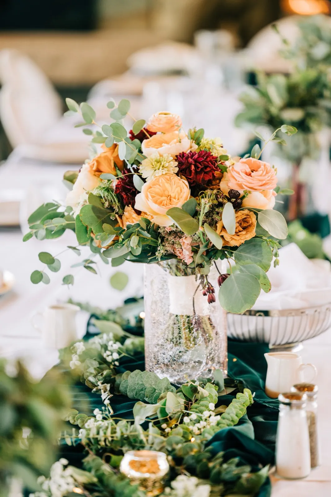 A centerpiece of peach garden roses, burgundy dahlias, and trailing eucalyptus on an emerald velvet runner — Tim Larsen Photography, Brainerd Lakes MN