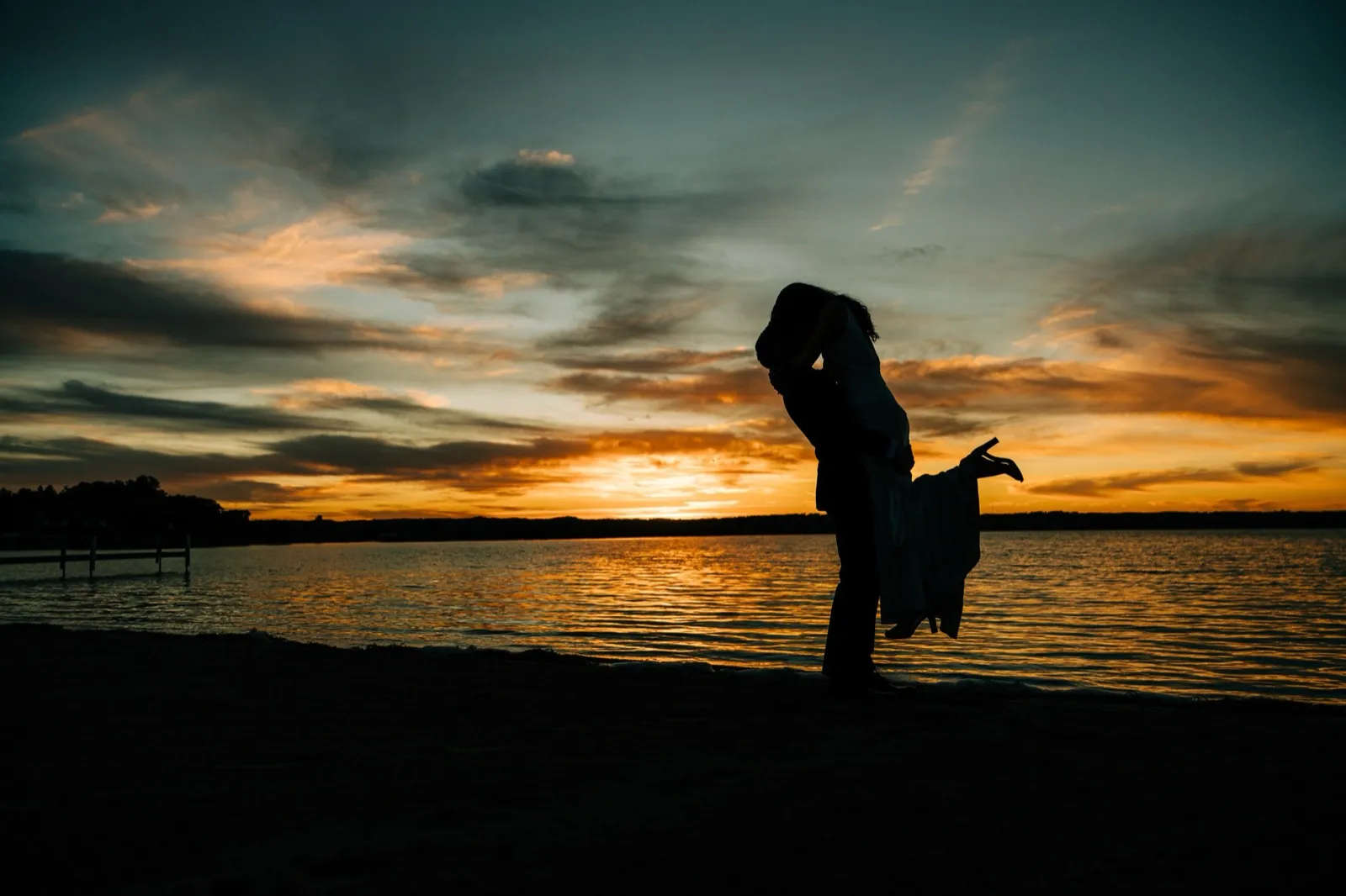 Josh lifts Madison in a kiss, both silhouetted against a vivid orange-and-teal sunset over Gull Lake at Madden's — Tim Larsen Photography, Brainerd Lakes MN