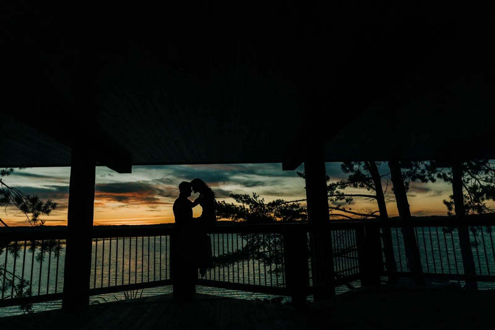 Madison and Josh stand forehead-to-forehead in silhouette on a covered porch over Gull Lake at dusk, an orange-and-blue sky behind — Tim Larsen Photography, Brainerd Lakes MN