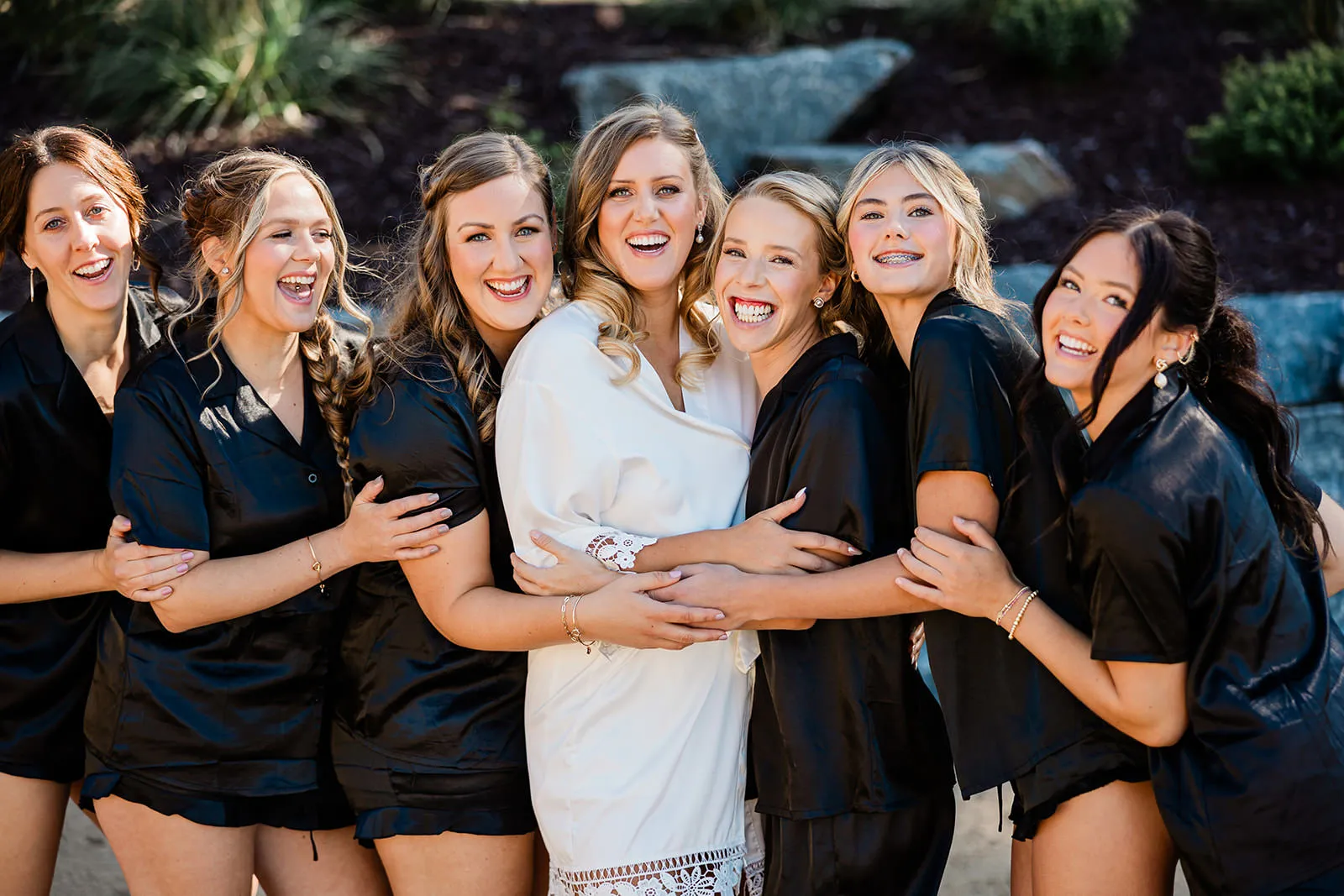 Bride and bridesmaids in black robes laughing together outside The Cove on Whitefish Lake