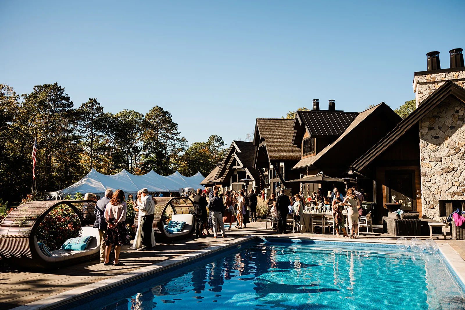 Cocktail hour by the pool at The Cove on Whitefish Lake — guests mingling with stone lodge behind