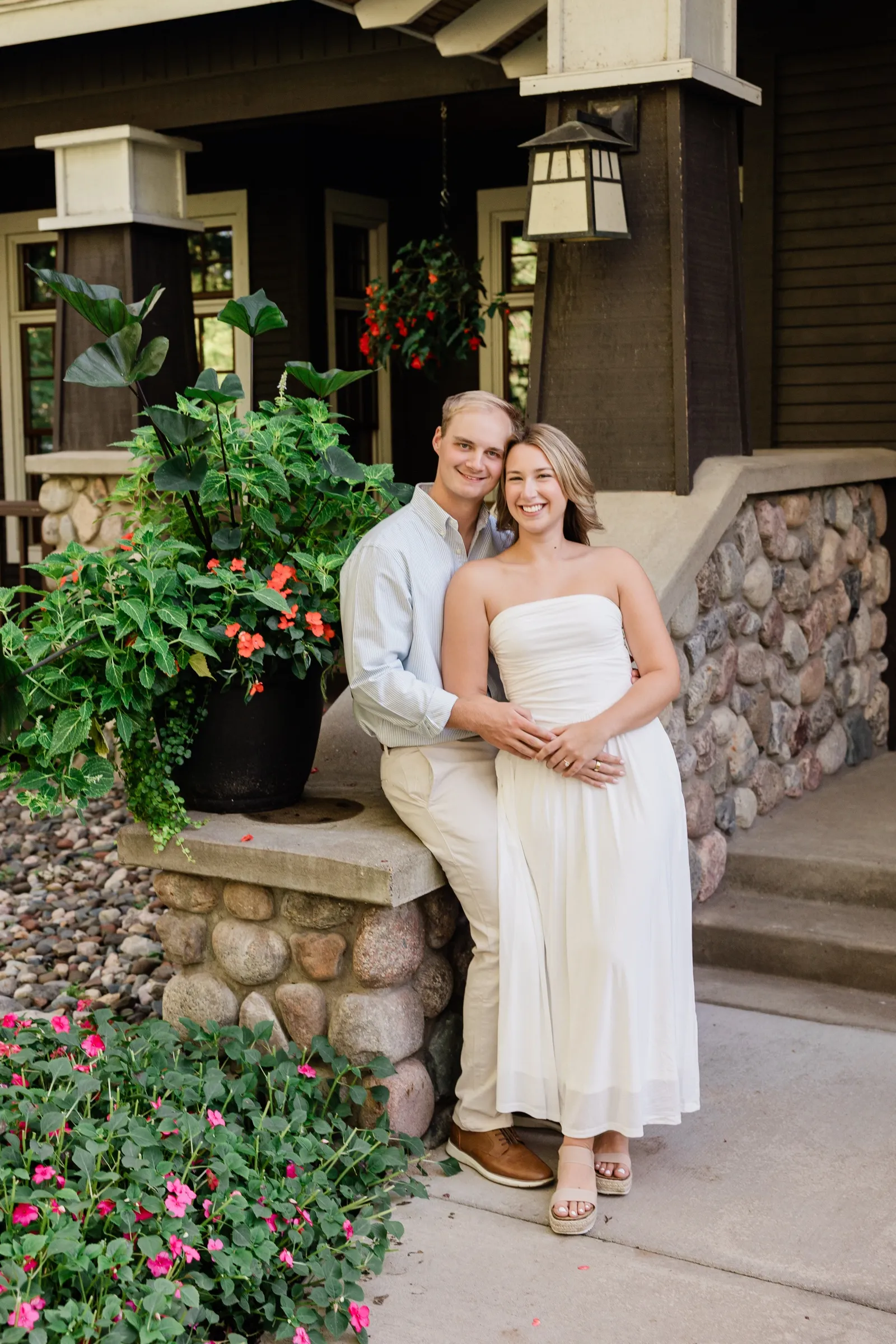 Olivia and Adam pose against the river-rock base of a craftsman porch surrounded by flowers — Tim Larsen Photography