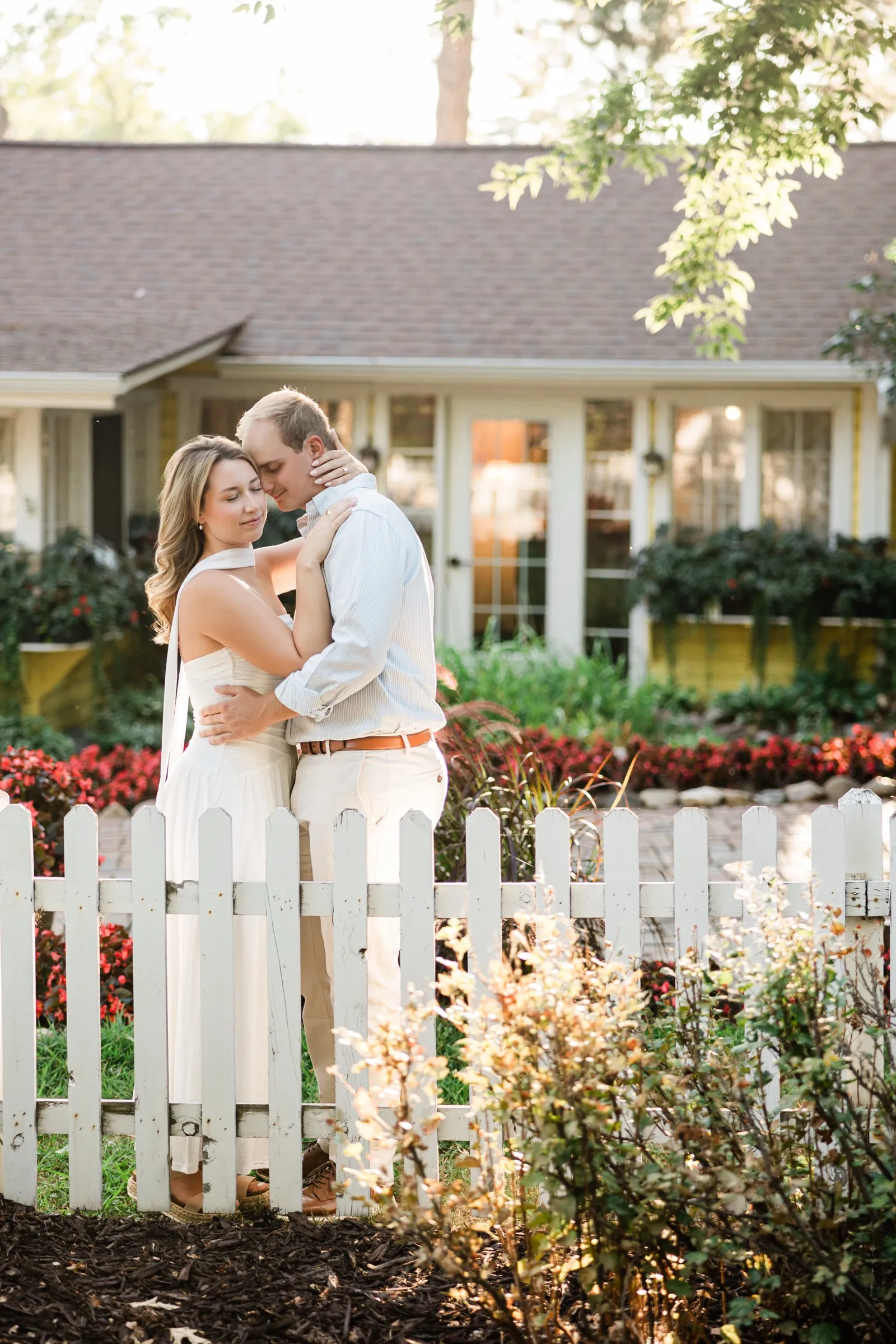 Olivia and Adam embrace in front of the yellow Italian Gardens restaurant, the picket fence soft in the foreground — Tim Larsen Photography