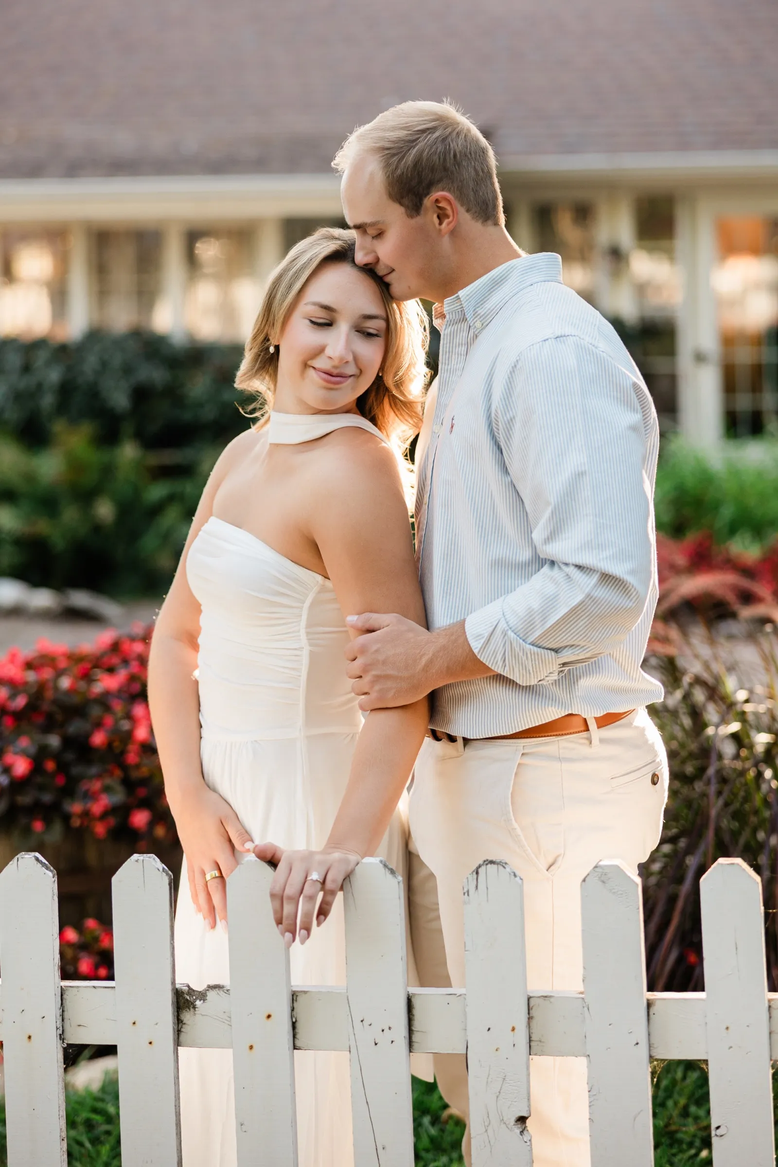 Olivia leans back into Adam at the picket fence while he kisses the top of her head — Tim Larsen Photography