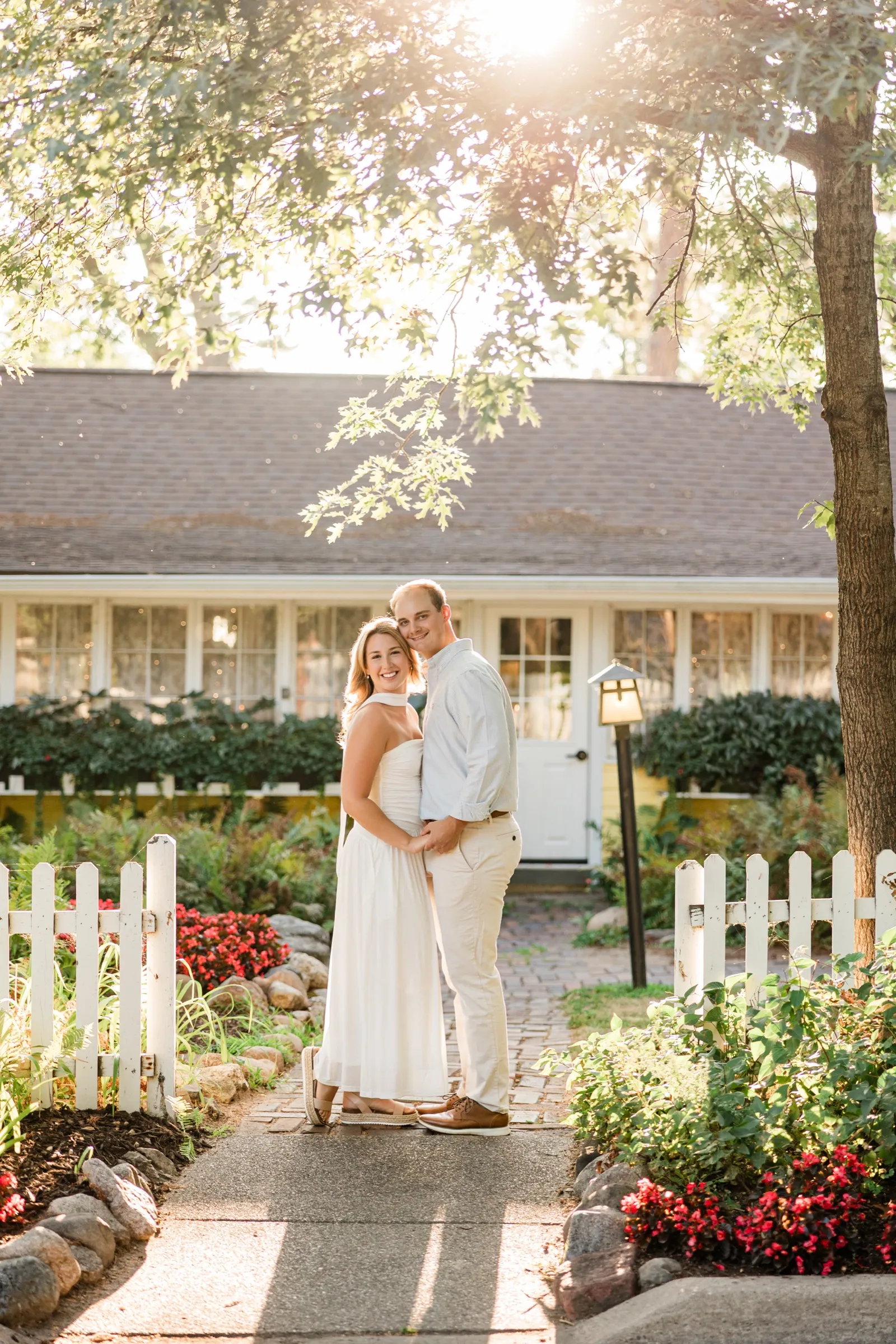 A wide golden-hour frame of Olivia and Adam on the garden path, sun flaring through the oaks above the Italian Gardens — Tim Larsen Photography