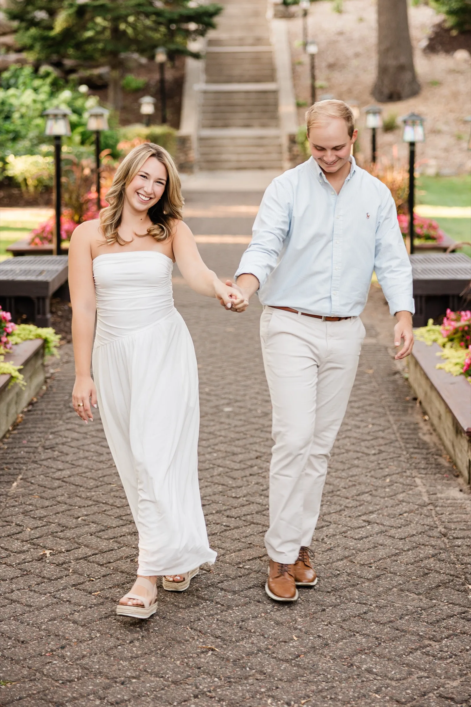 Olivia and Adam walk hand in hand down the lantern-lined garden path, both laughing — Tim Larsen Photography