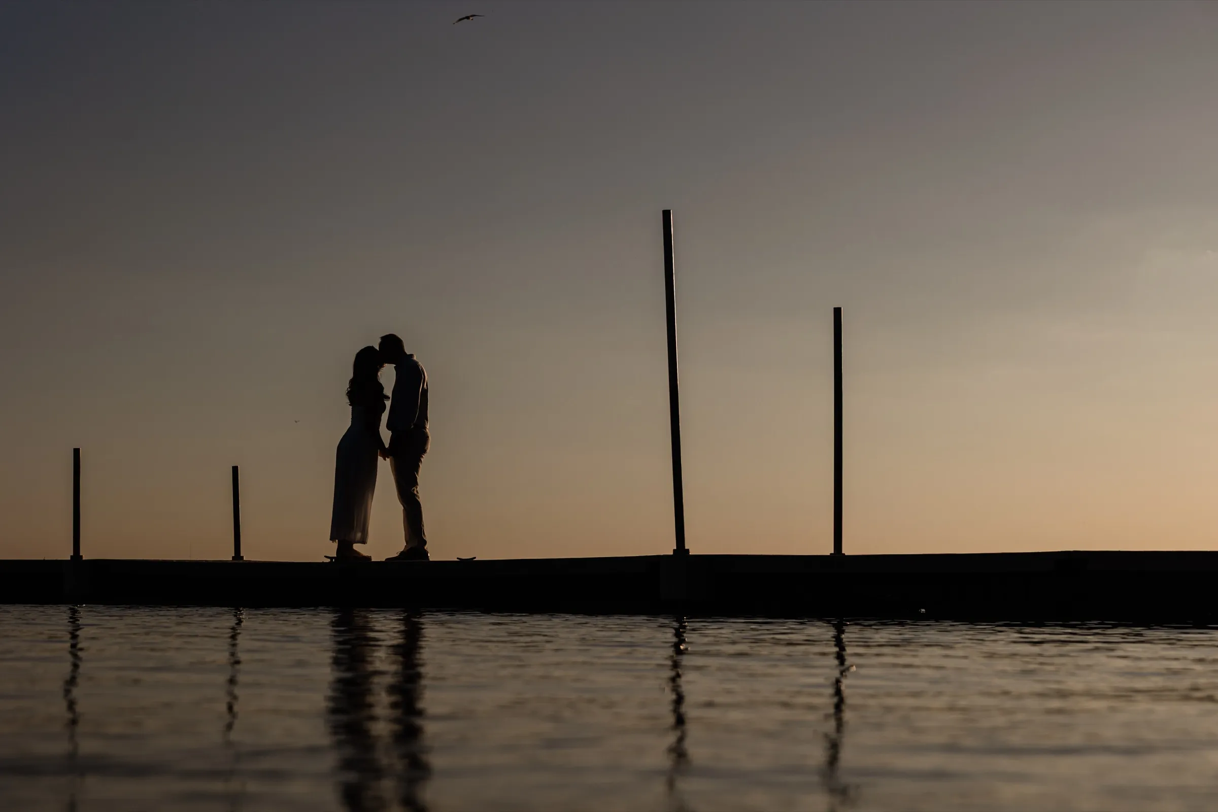 Olivia and Adam kiss in silhouette on the Gull Lake dock at dusk, mirrored in the calm water — Tim Larsen Photography