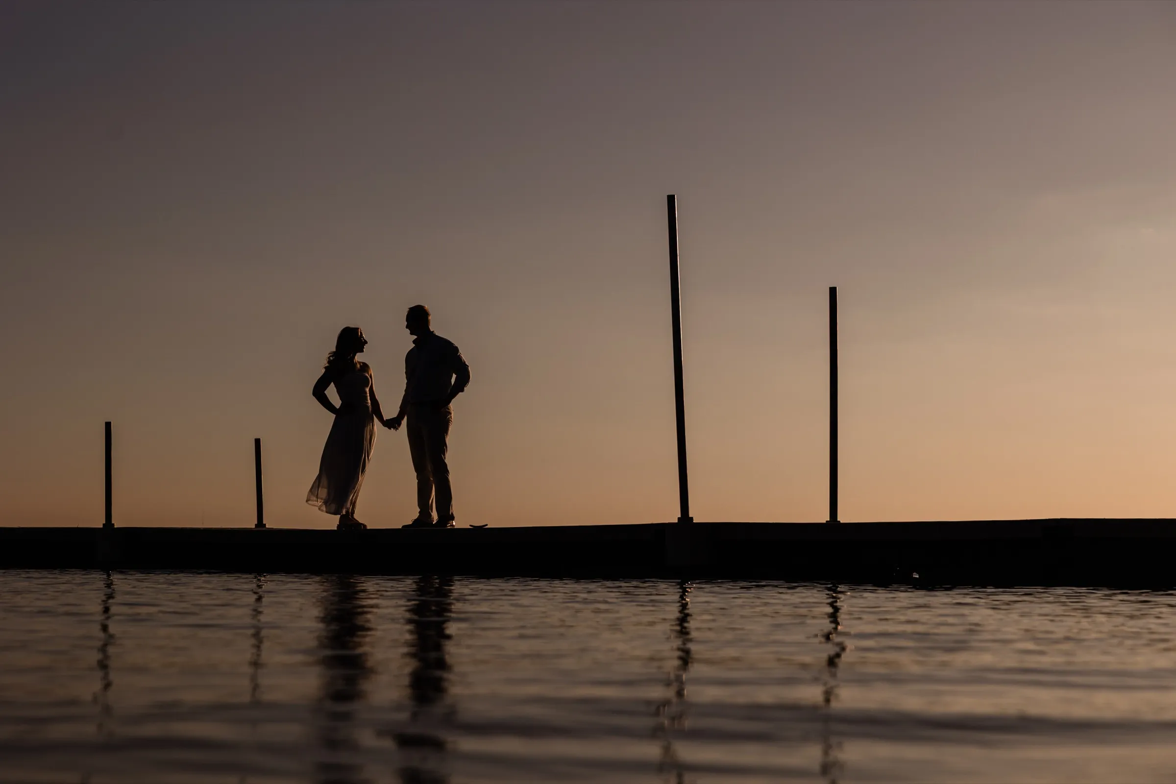 Olivia and Adam hold hands in silhouette on the dock, the dusk sky reflected in Gull Lake — Tim Larsen Photography