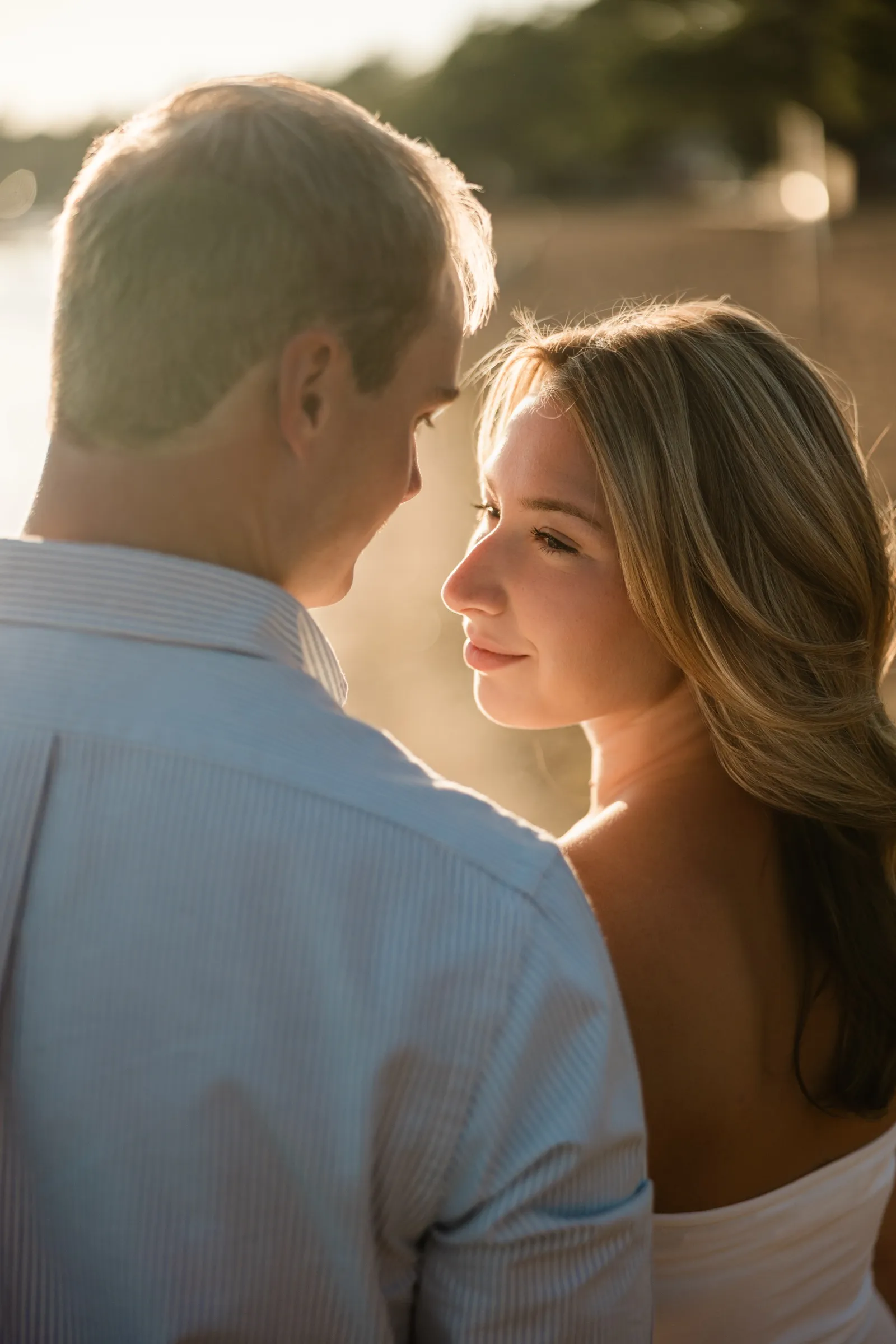 Over Adam's shoulder, Olivia gazes at him with golden backlit hair on the Gull Lake shore — Tim Larsen Photography