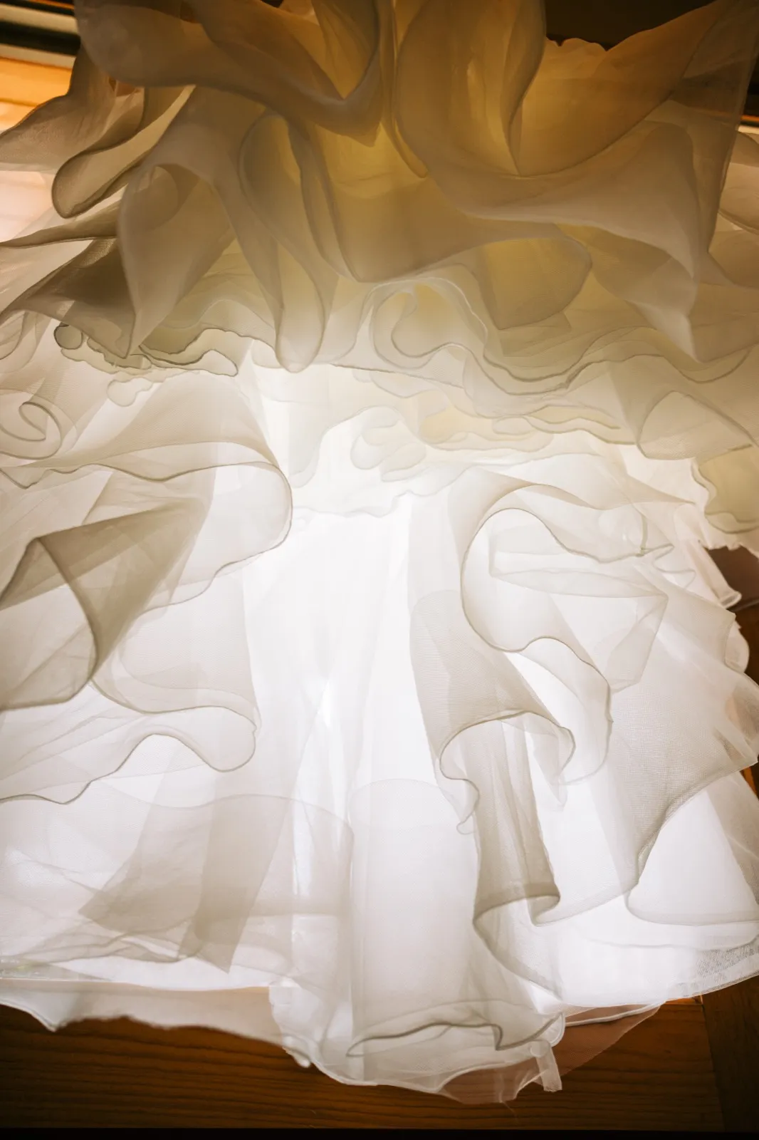 An abstract upward view through the layered tulle skirt of a wedding gown, backlit by warm window light revealing the fabric's translucent folds. — Tim Larsen Photography, Brainerd Lakes MN