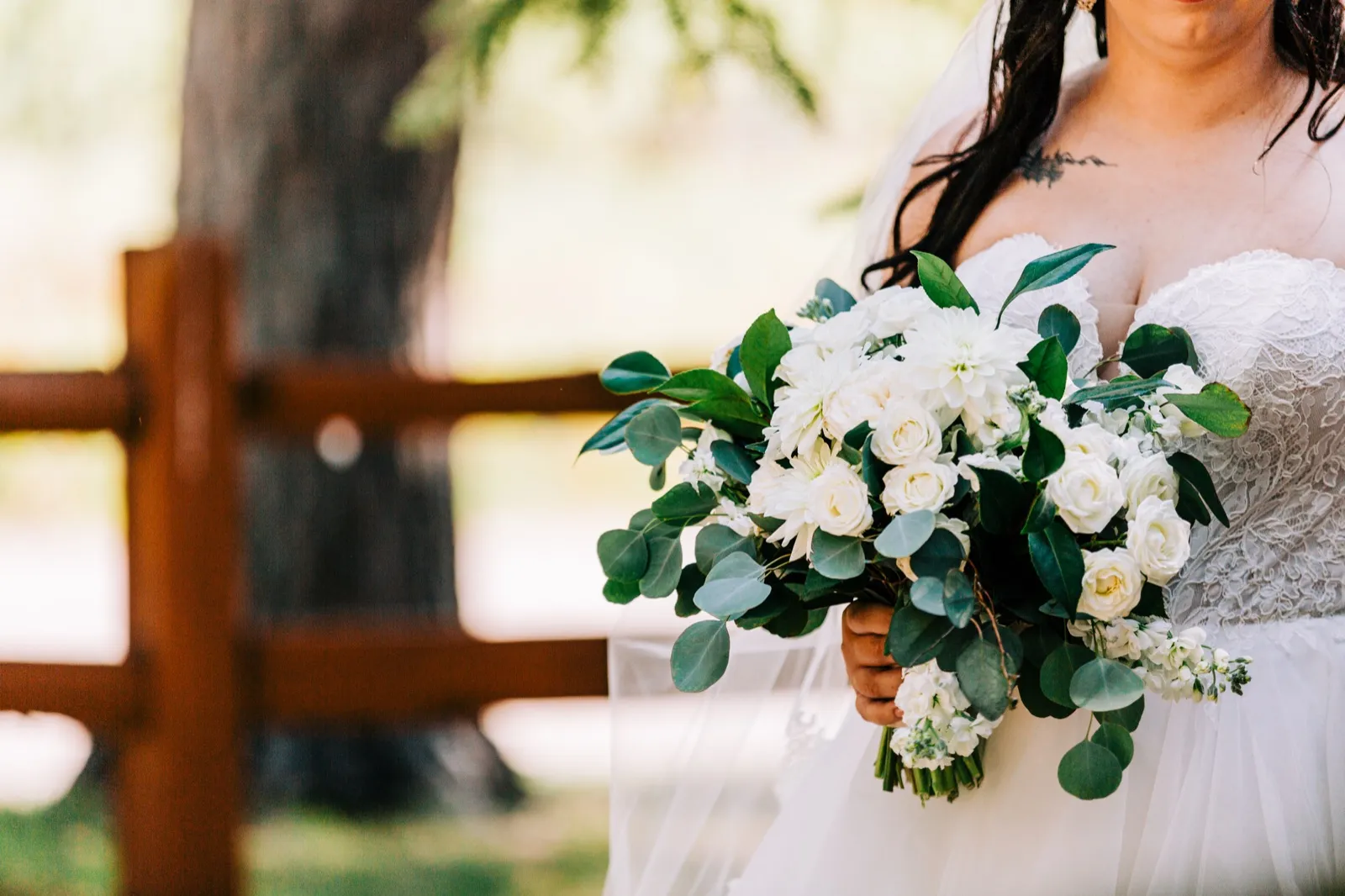 The bride holds a lush white-and-green bouquet of roses, dahlias, and eucalyptus in front of a rustic wooden fence — Tim Larsen Photography, Brainerd Lakes MN