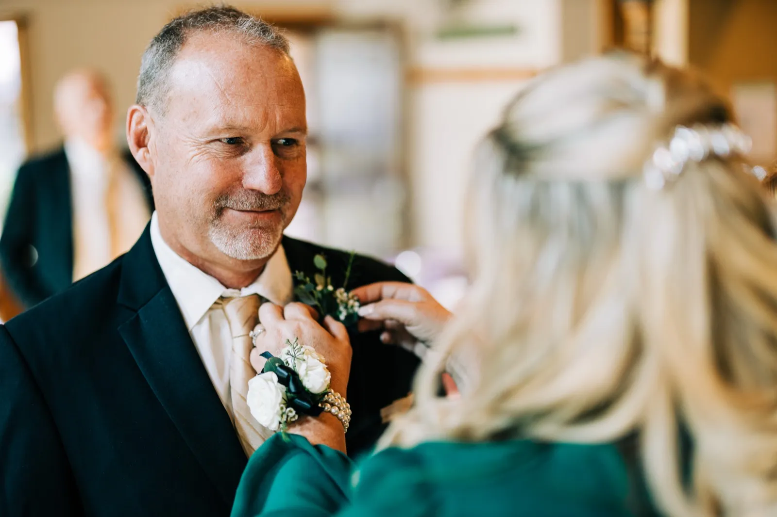 The father of the bride smiles softly as his daughter pins a white boutonniere to his navy suit jacket — Tim Larsen Photography, Brainerd Lakes MN