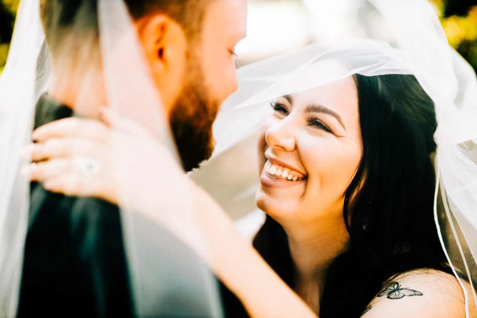 The bride laughs broadly at her groom beneath a sunlit veil that frames both their faces — Tim Larsen Photography, Brainerd Lakes MN