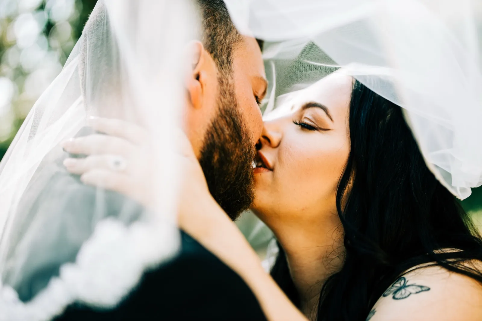The couple kisses beneath the bride's veil, her hand with engagement ring resting on his cheek as soft light filters through the tulle — Tim Larsen Photography, Brainerd Lakes MN