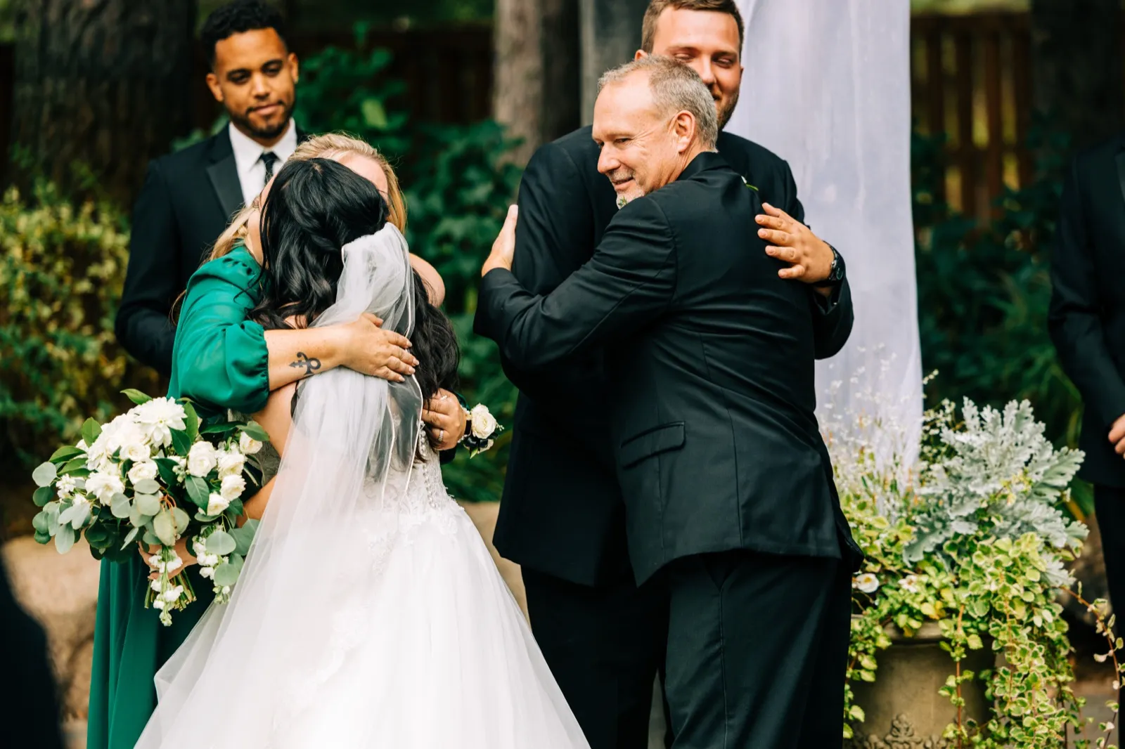 The bride and her father embrace family members at the end of the ceremony aisle while the groom and groomsman look on smiling — Tim Larsen Photography, Brainerd Lakes MN