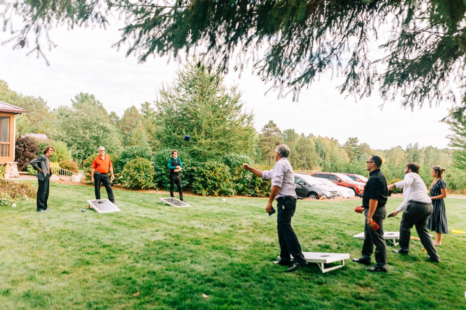 Wedding guests play cornhole on a lawn at Pine Peaks Event Center, with a bean bag caught mid-air between two boards — Tim Larsen Photography, Brainerd Lakes MN