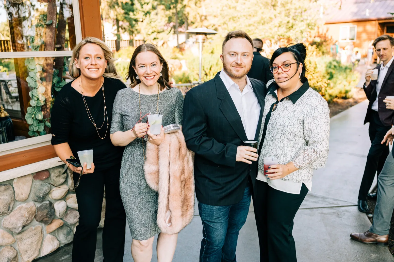 Four wedding guests pose together with cocktails on a stone patio in warm late-afternoon light — Tim Larsen Photography, Brainerd Lakes MN