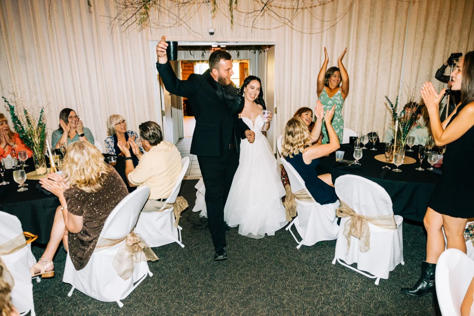 Taylor and Charles enter their reception with arms raised as guests on both sides clap and cheer. — Tim Larsen Photography, Brainerd Lakes MN