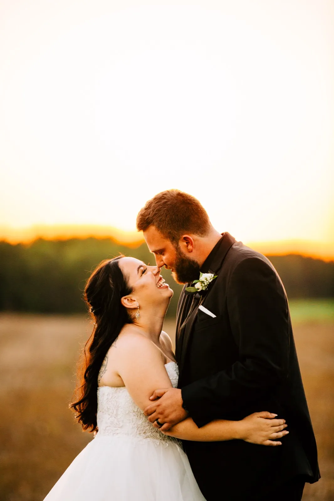 The bride throws her head back laughing as the groom leans in close, both backlit by a golden sunset over an open field — Tim Larsen Photography, Brainerd Lakes MN