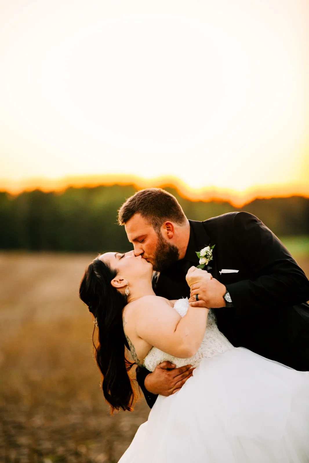 The groom dips the bride backward into a kiss in an open field as the sun sets behind a distant treeline — Tim Larsen Photography, Brainerd Lakes MN