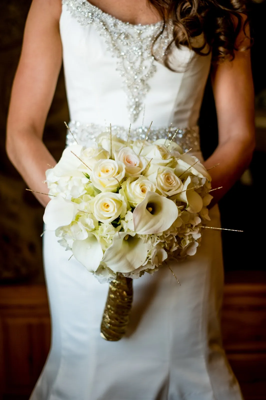 The bride holds a white rose and calla lily bouquet with gold accents against her beaded ivory gown. — Tim Larsen Photography, Brainerd Lakes MN